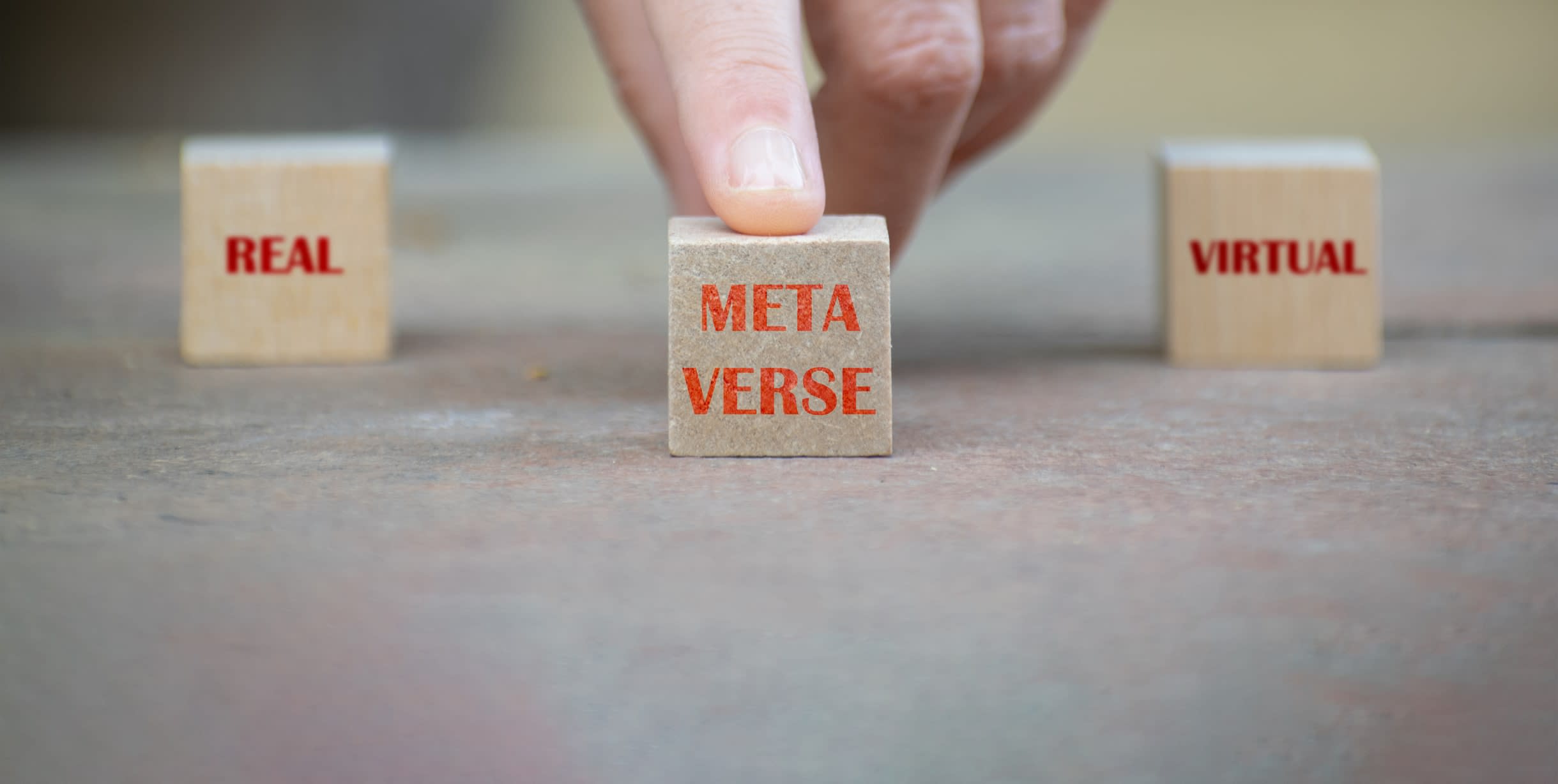 Finger on a block with the word 'metaverse', flanked by others reading 'virtual' and 'real'