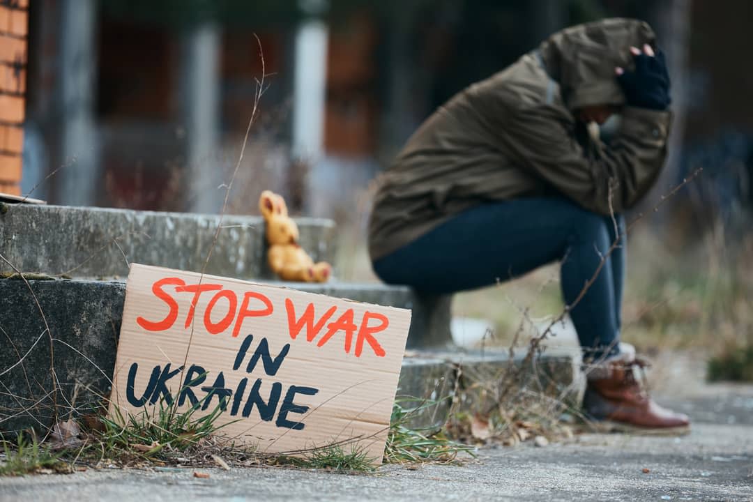 Ukraine woman sits with her head in her hands on steps with a sign saying: Stop war in Ukraine