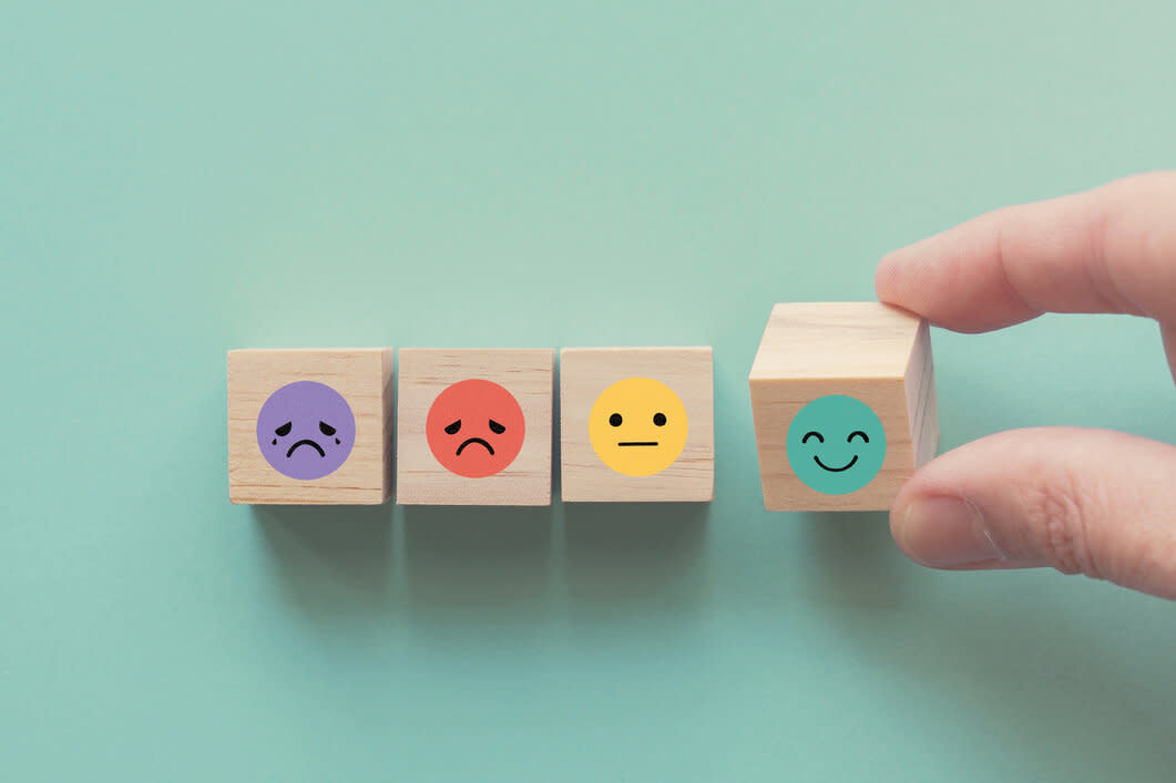 Hand choosing smiley-face wooden block beside others with sad and neutral faces