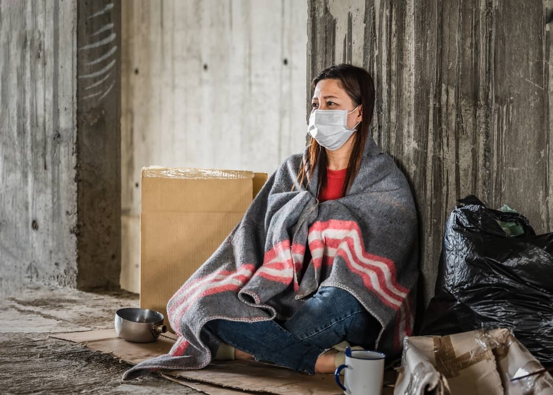 A woman sits on a street wrapped in a blanket.