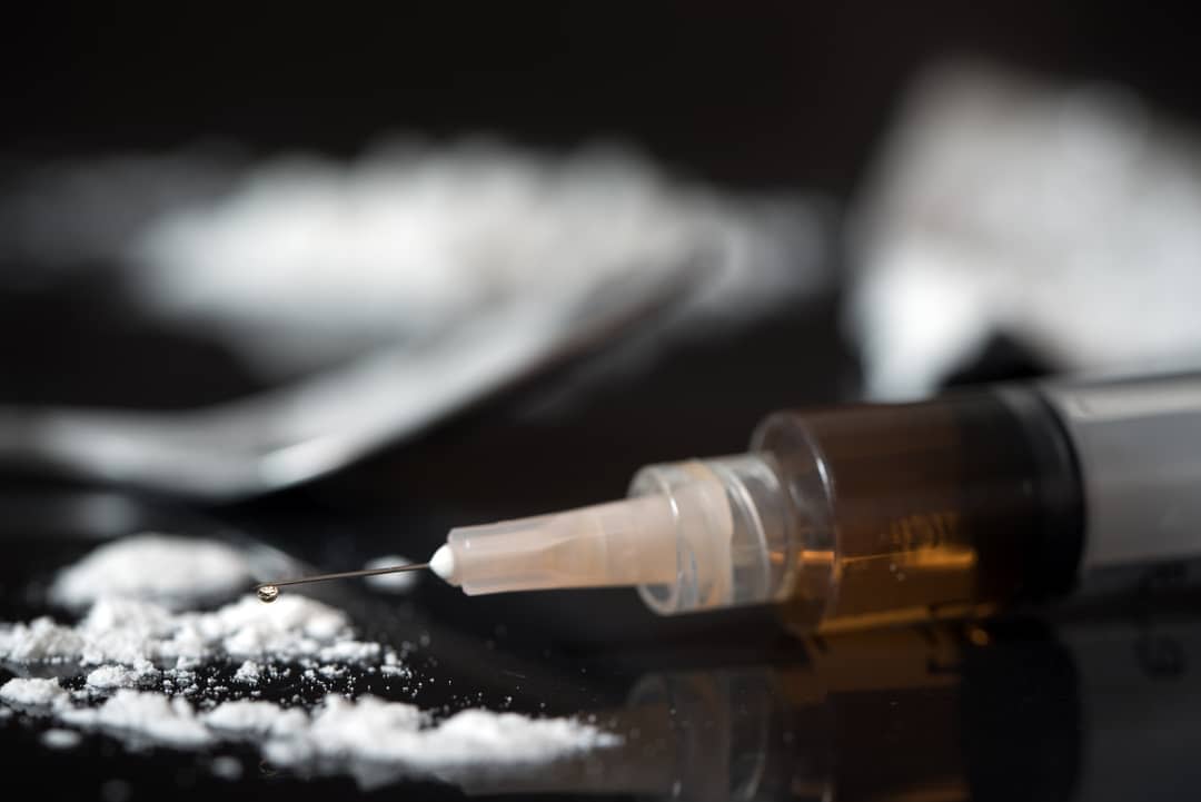 A syringe filled with heroin, sitting next to a white powder 