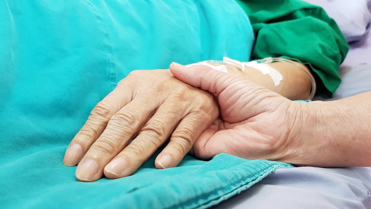 Close-up shot of a doctor holding a patient's hand in a hospital bed.