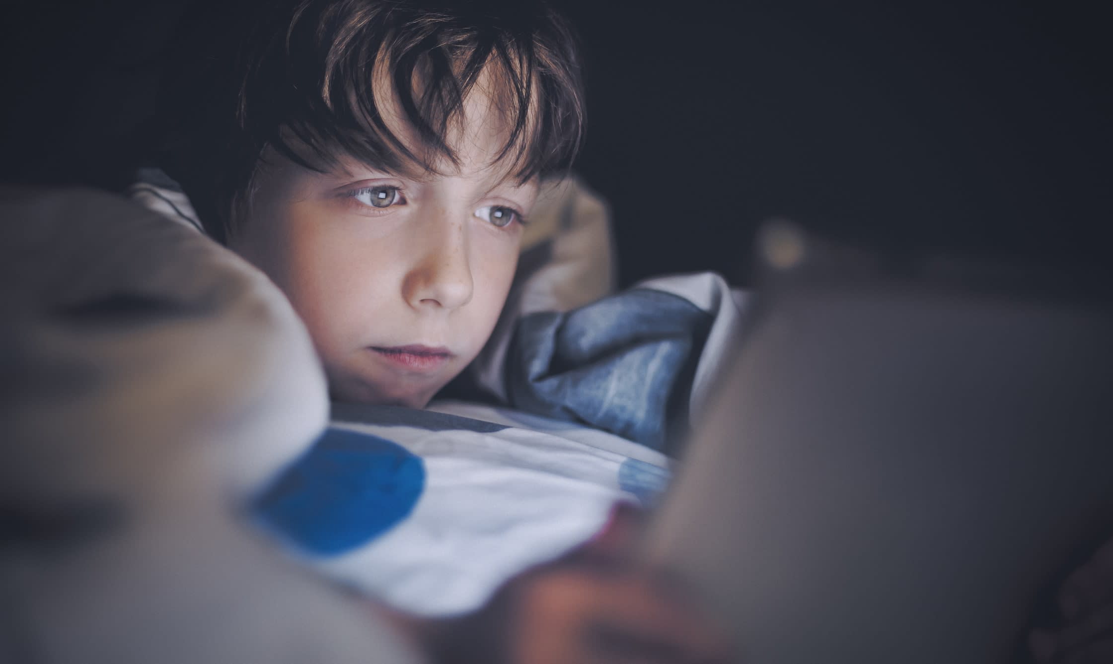 Boy laying in bed and staring at a digital tablet