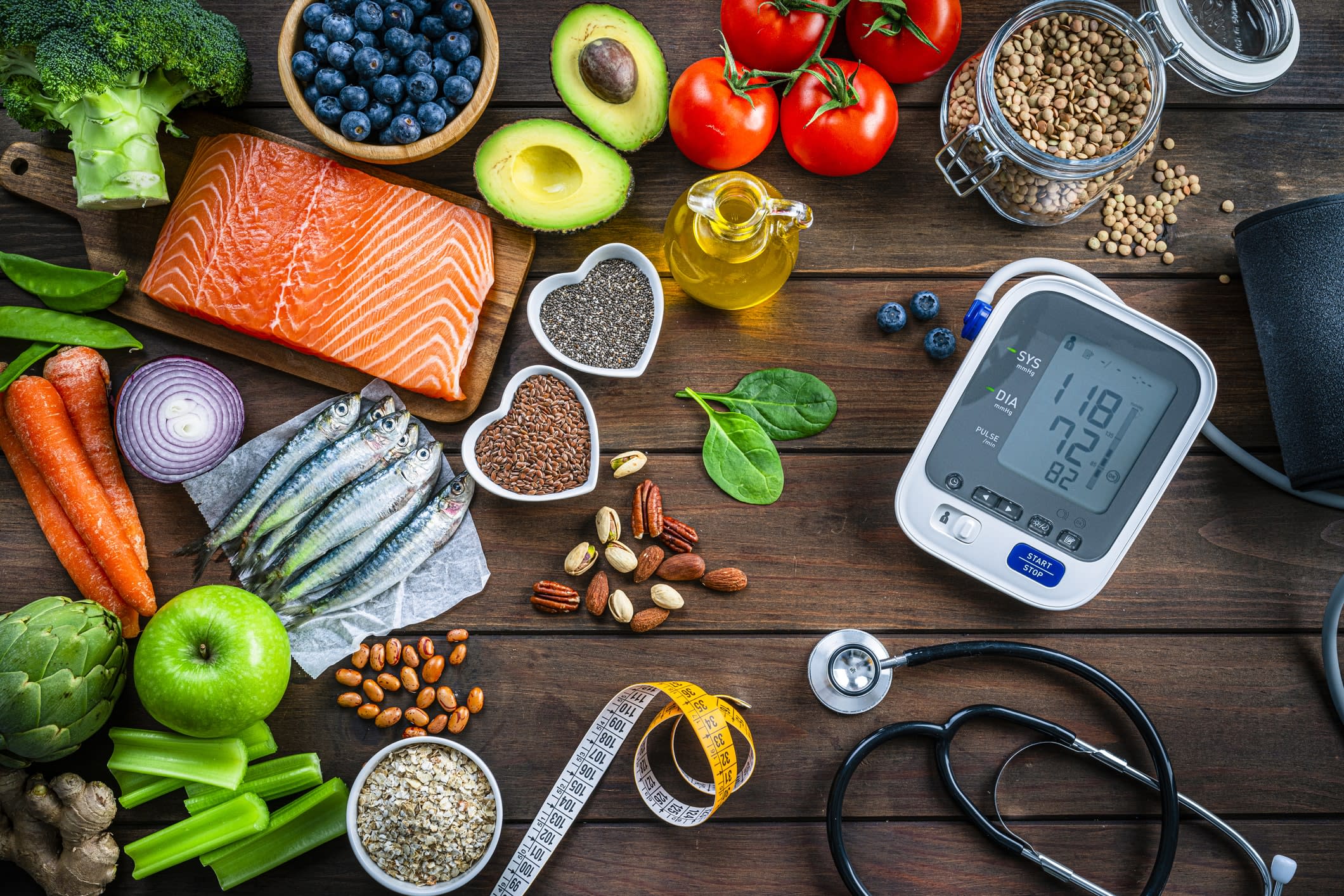 A table with fresh fruit, fish, vegetables, and a heart pressure monitor and measuring tape