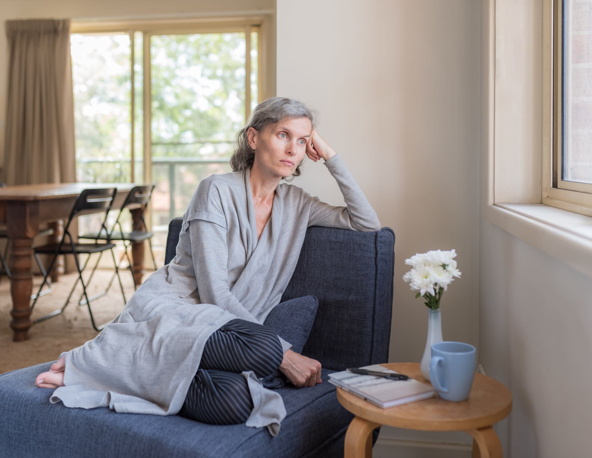 A sad, middle aged woman sitting on chair in living room looking out window