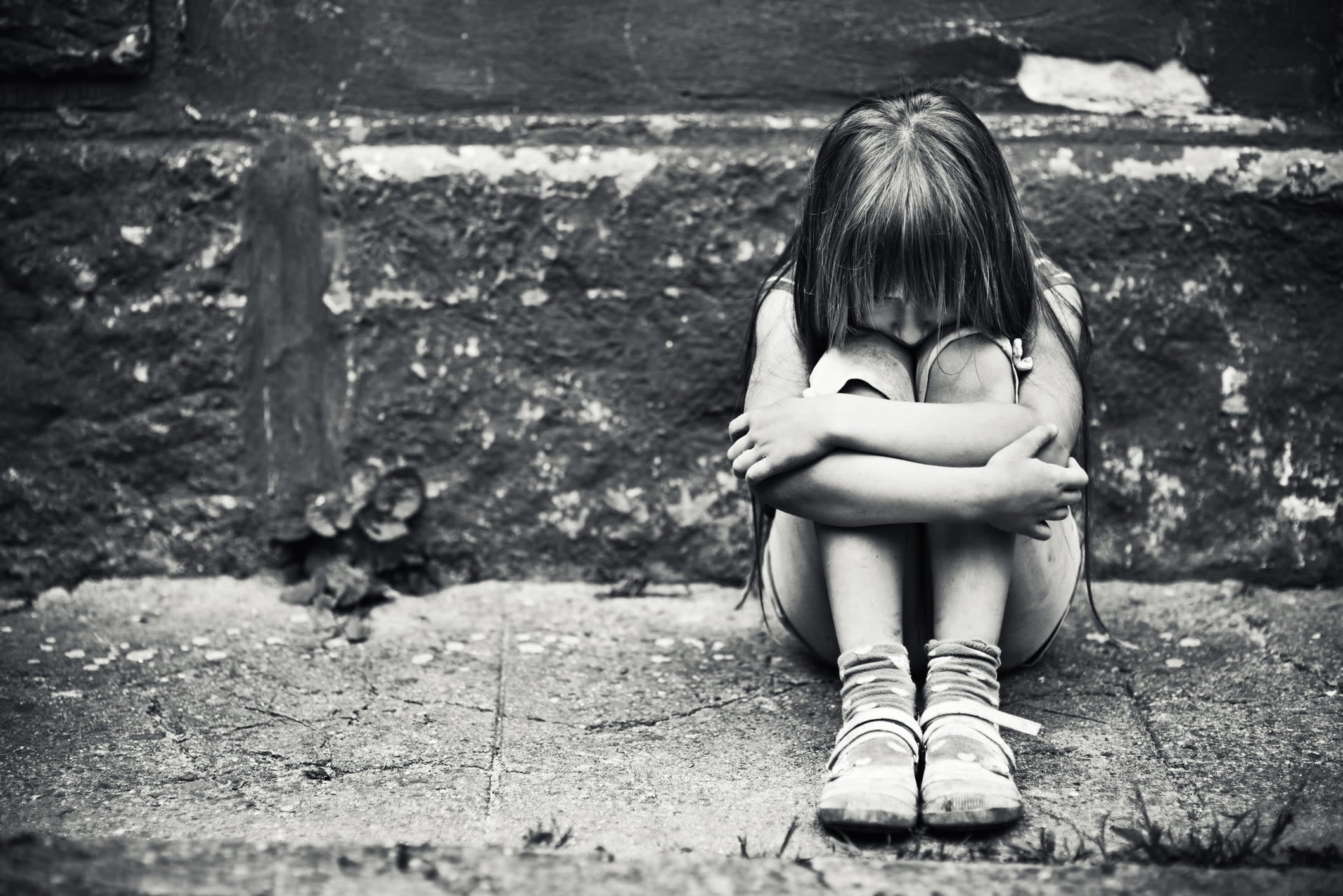 Black-and-white image of a sad-looking girl cluthcing her knees to her chest