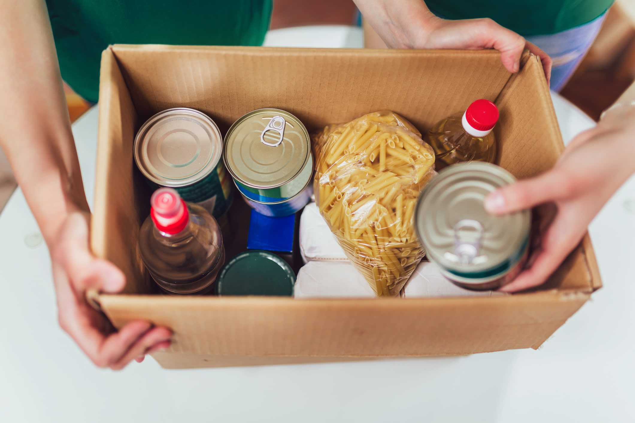 Hands putting donated food goods into a cardboard box