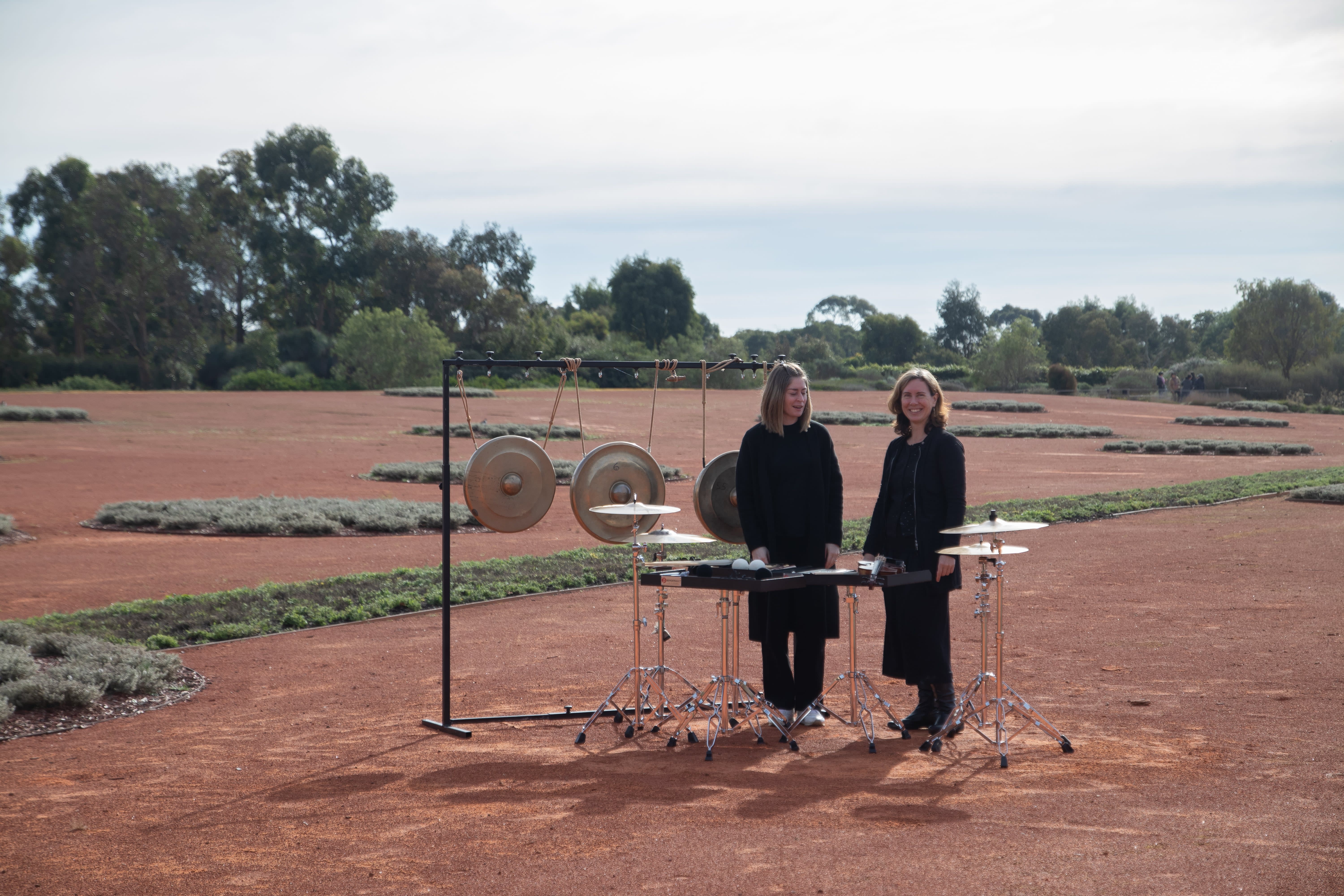 Louise Devenish and Anna McMichael standing outdoors with perscussion instruments at Royal Botanic Gardens Cranbourne, Melbourne