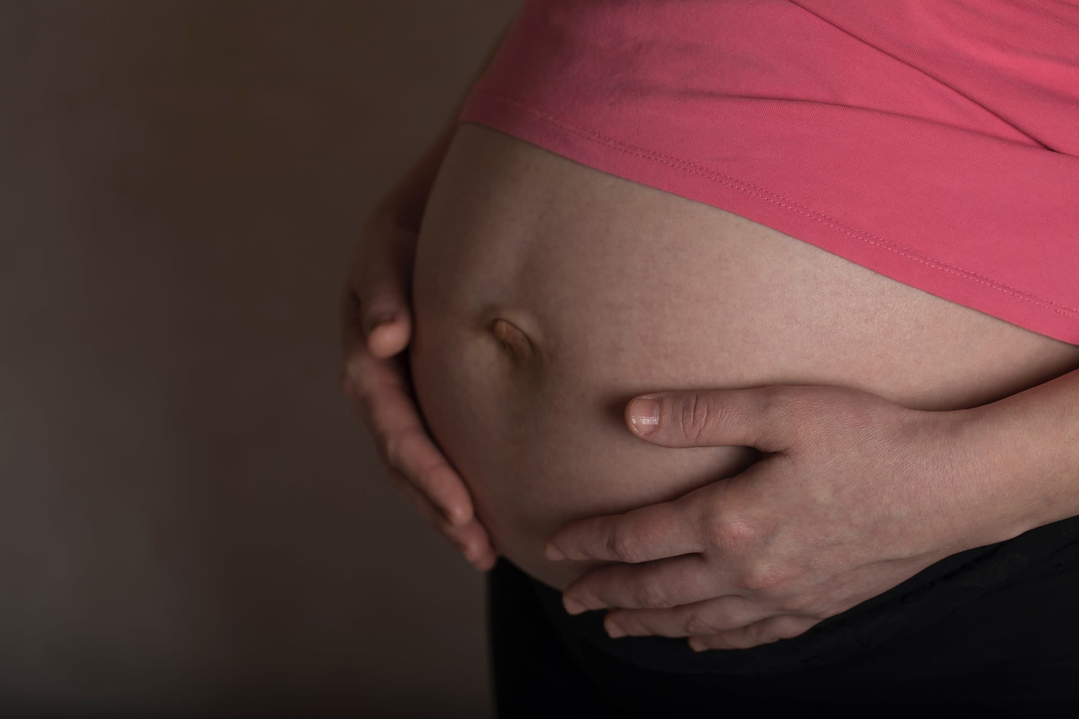 Close-up of a woman's hands on her exposed pregnant belly.