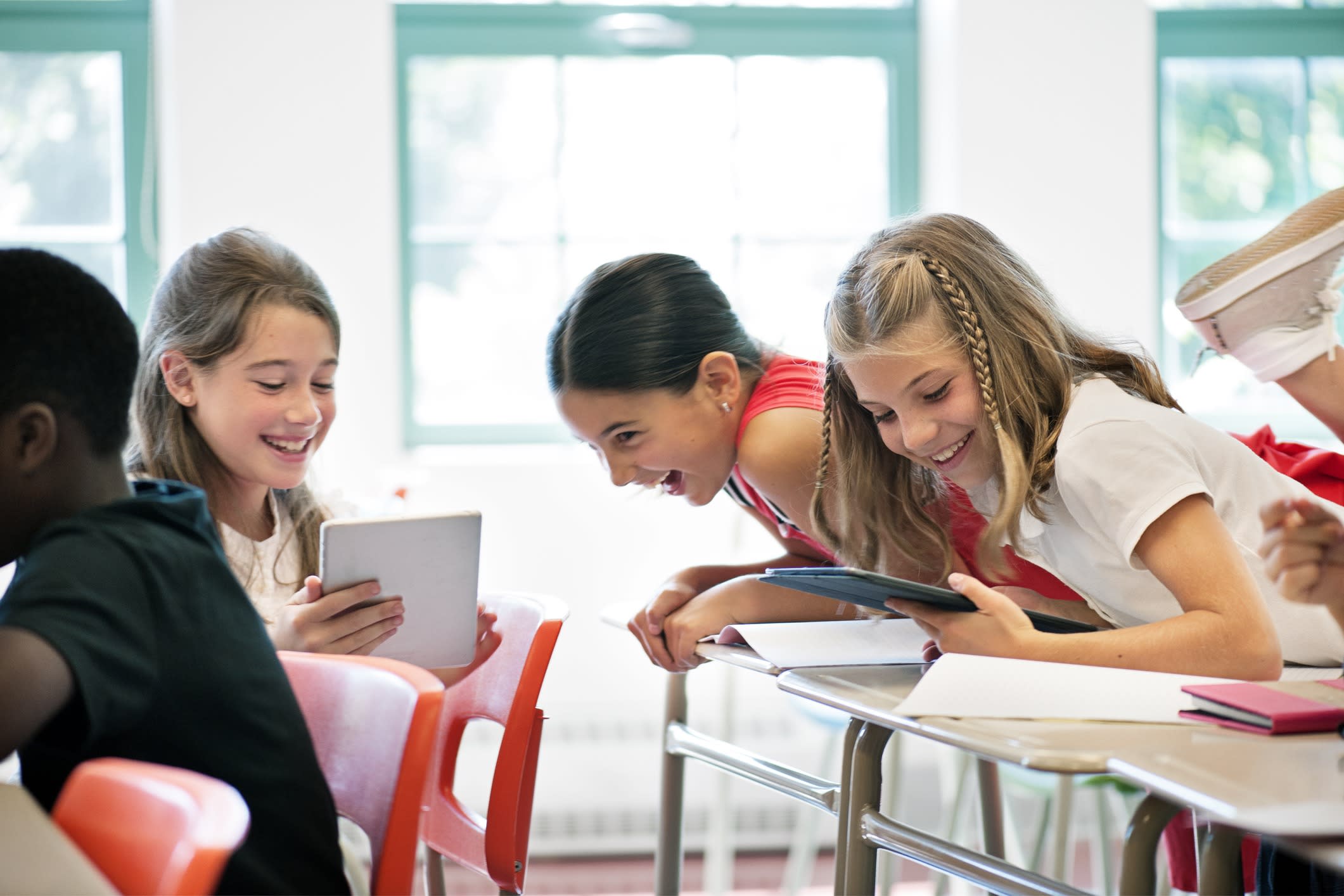 Young girls in a classroom talking and looking at an ipad.