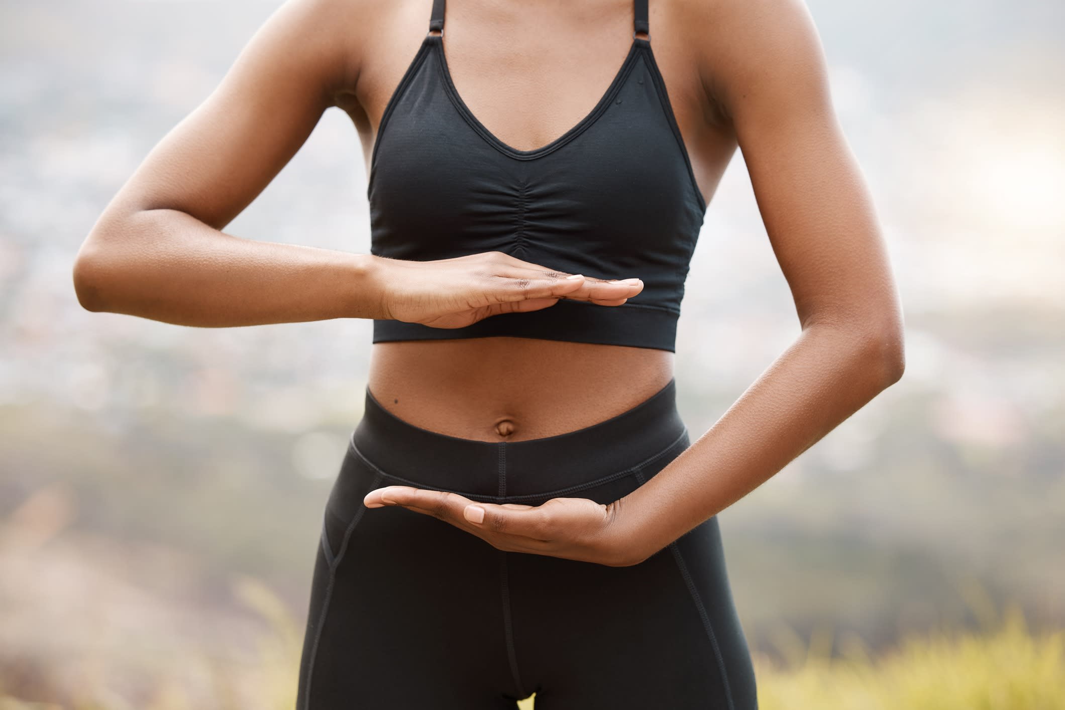 Young woman framing her stomach with her hands while standing outside in nature.