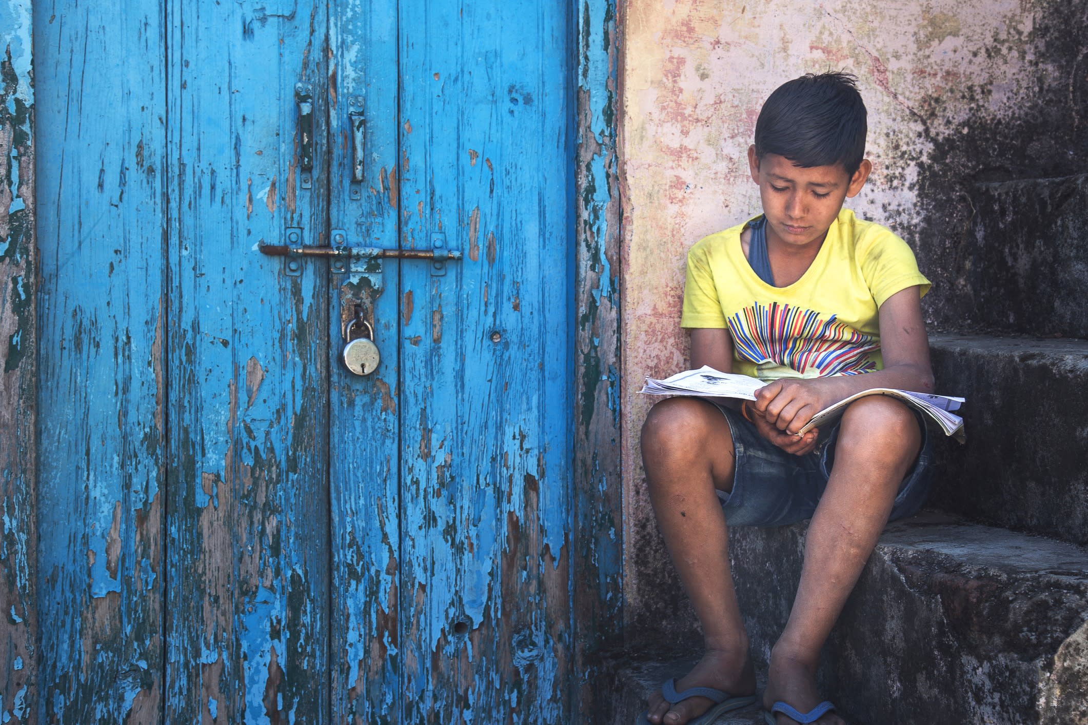 Boy sitting on steps near the door with rusty lock and reading