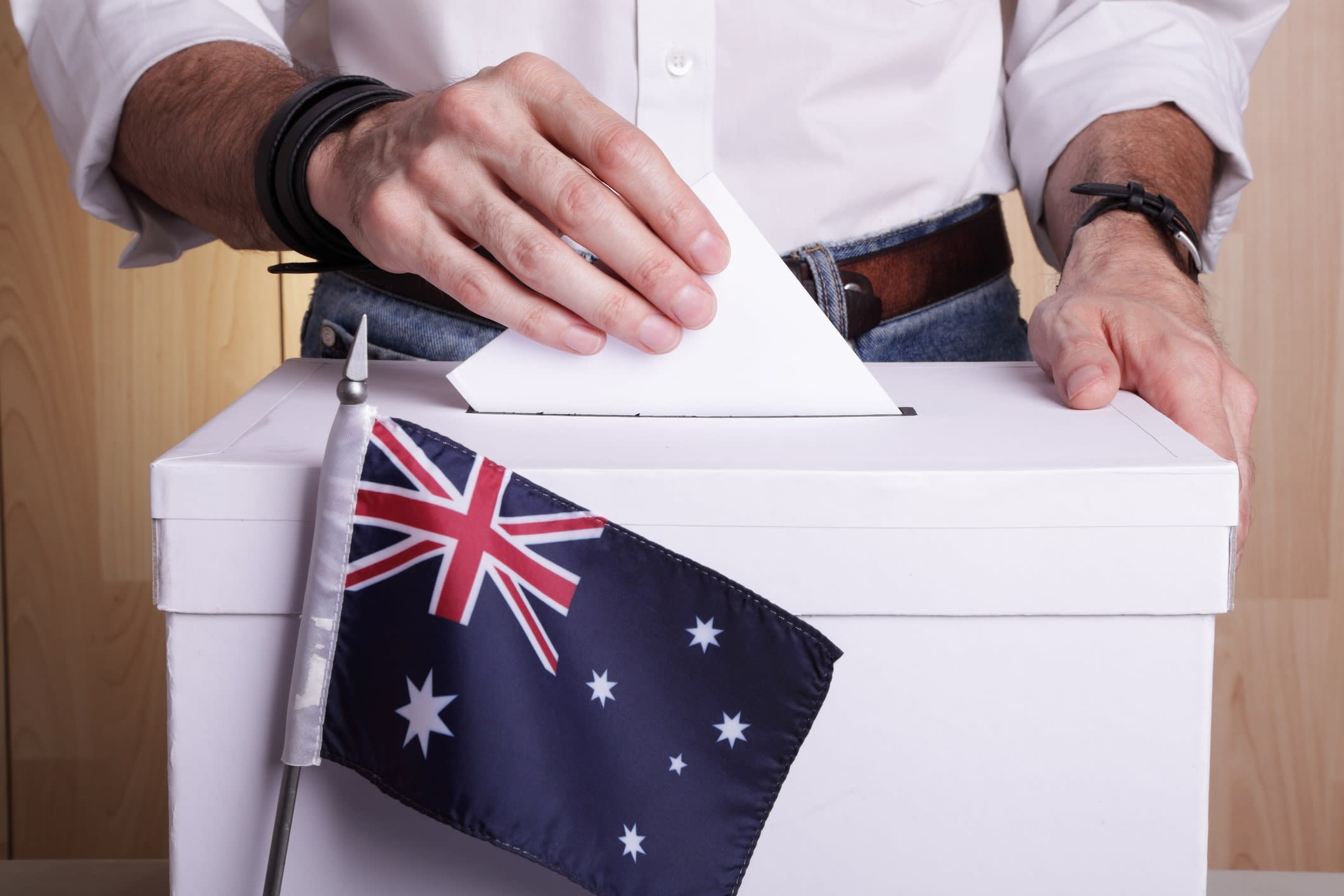 Man putting a ballot paper into a white box sitting behind a small Australian flag