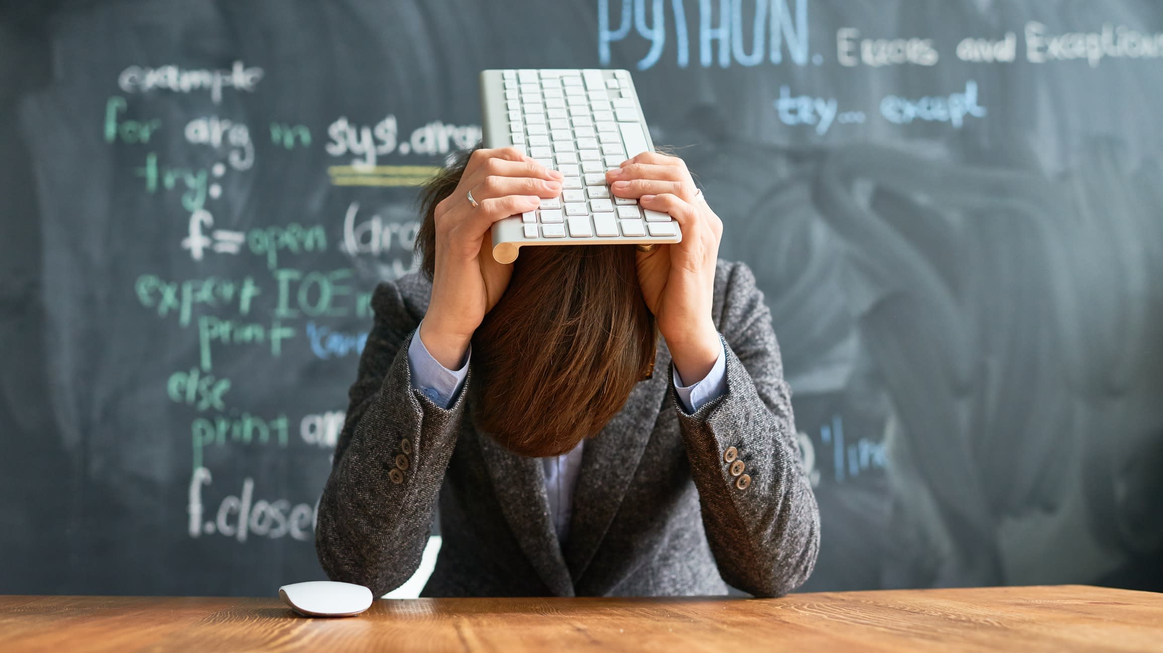 Frustrated exhausted female computer programmer beating herself with computer keyboard