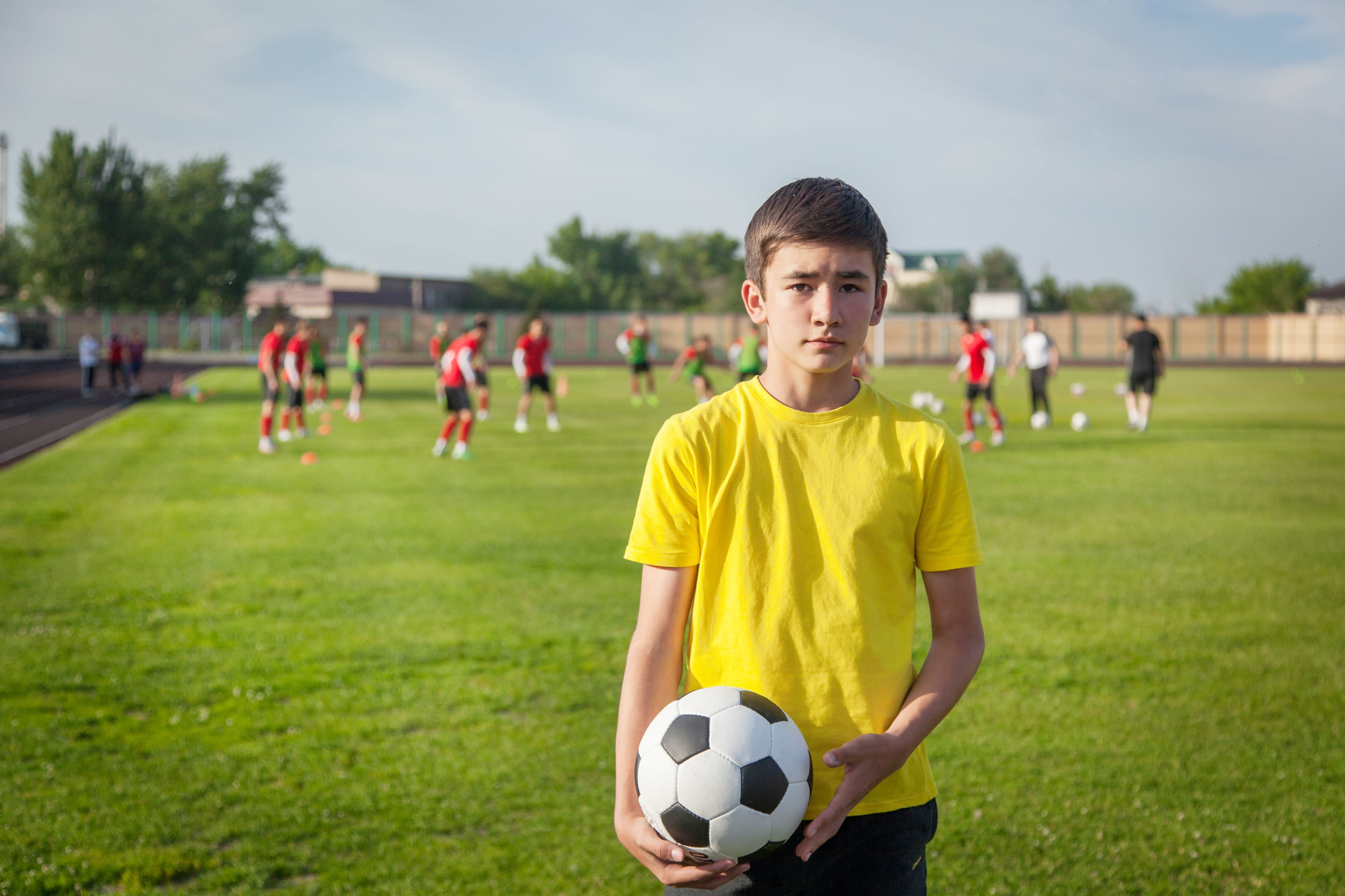 Boy in a yellow shirt on a football field holding a soccer balls.