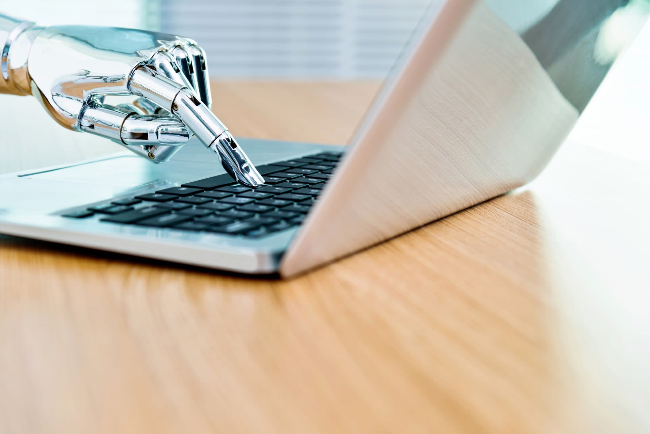 Robot's shiny silver hand typing on laptop keyboard.