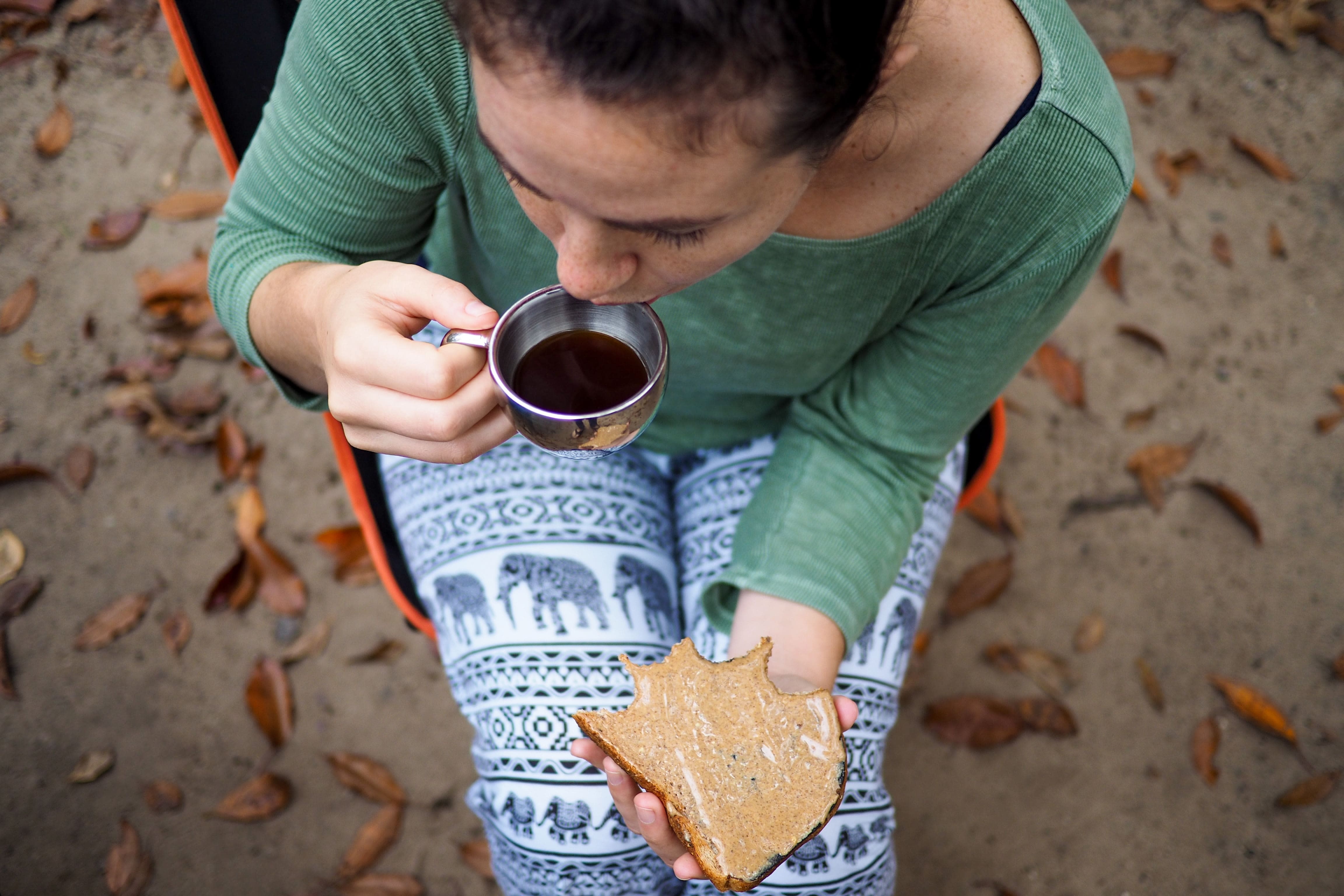 Woman photographed from above sipping black coffe and eating a plain slice of bread