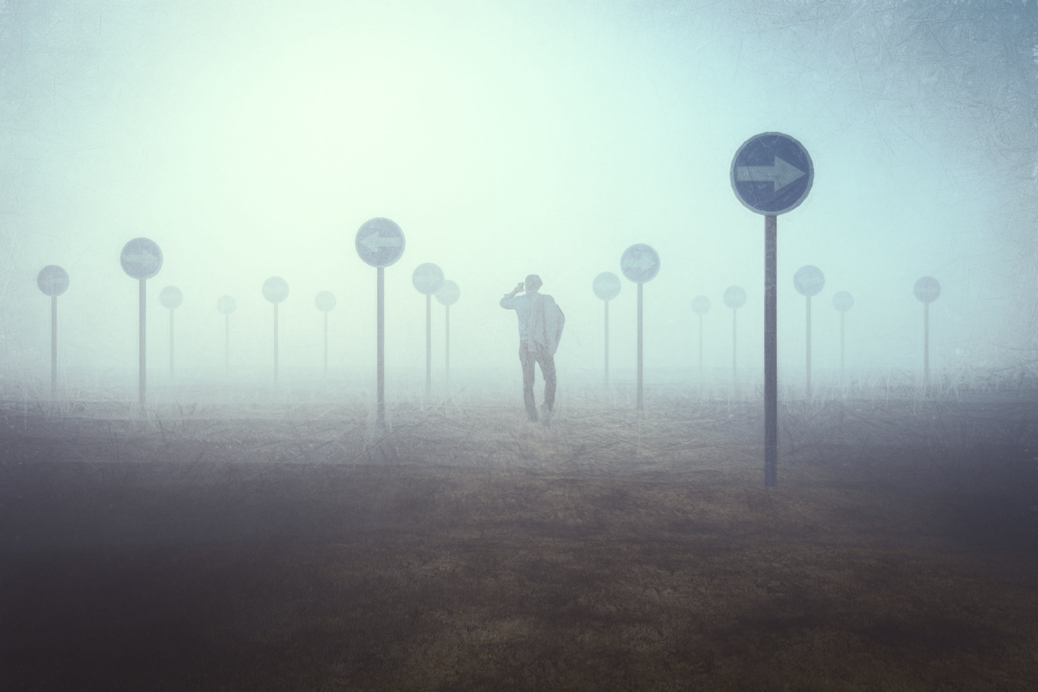 A man among signs pointing in different directions against a grey background.