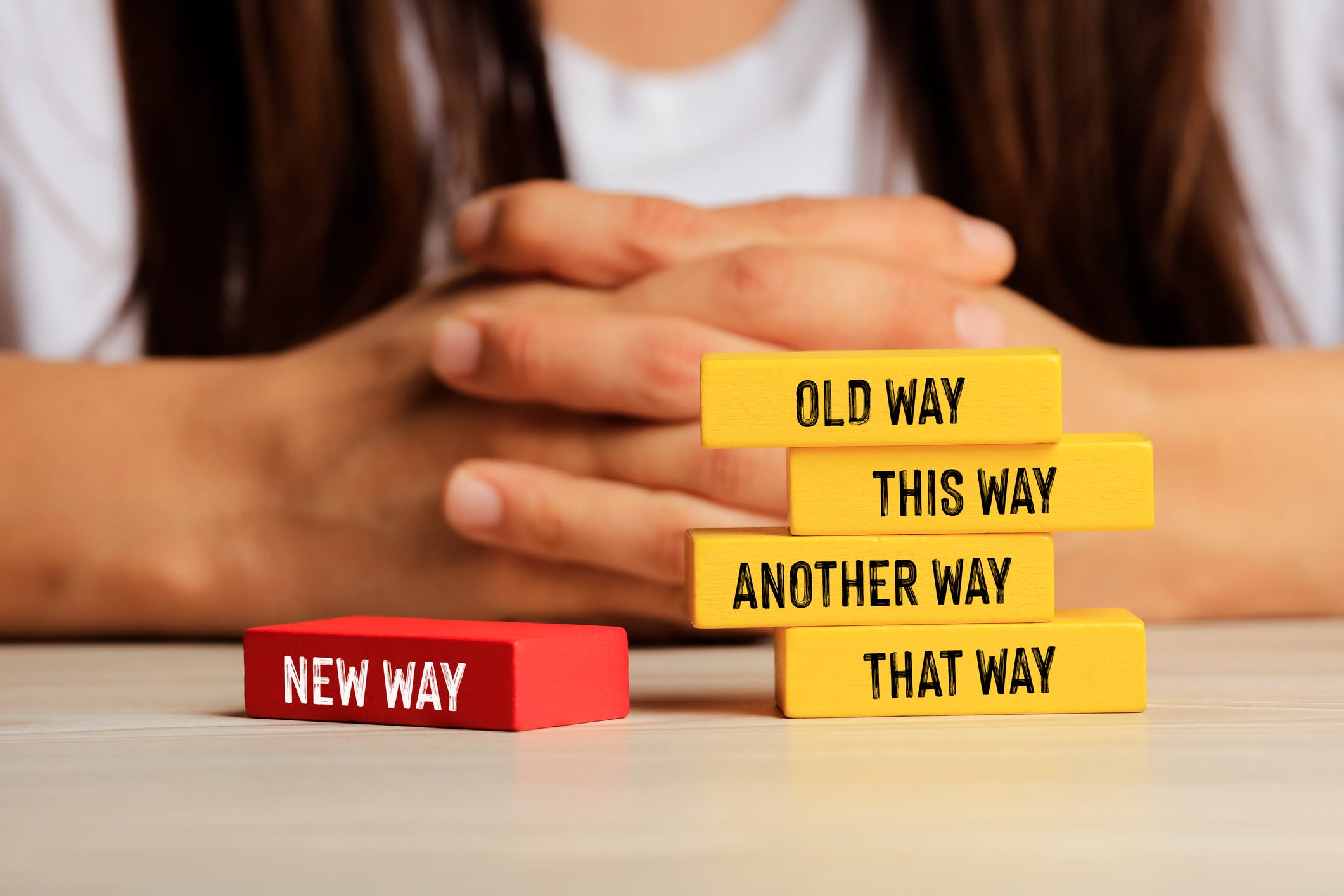 Man sits at a desk with his hands folded behind wooden block signs showing a new way to do things.