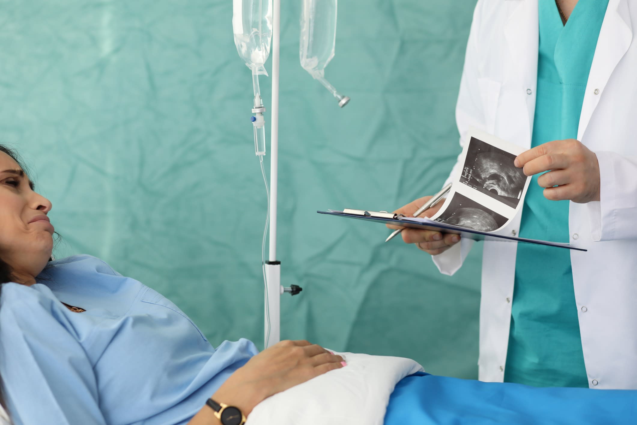 A doctor holding an ultrasound image talks with a female patient.