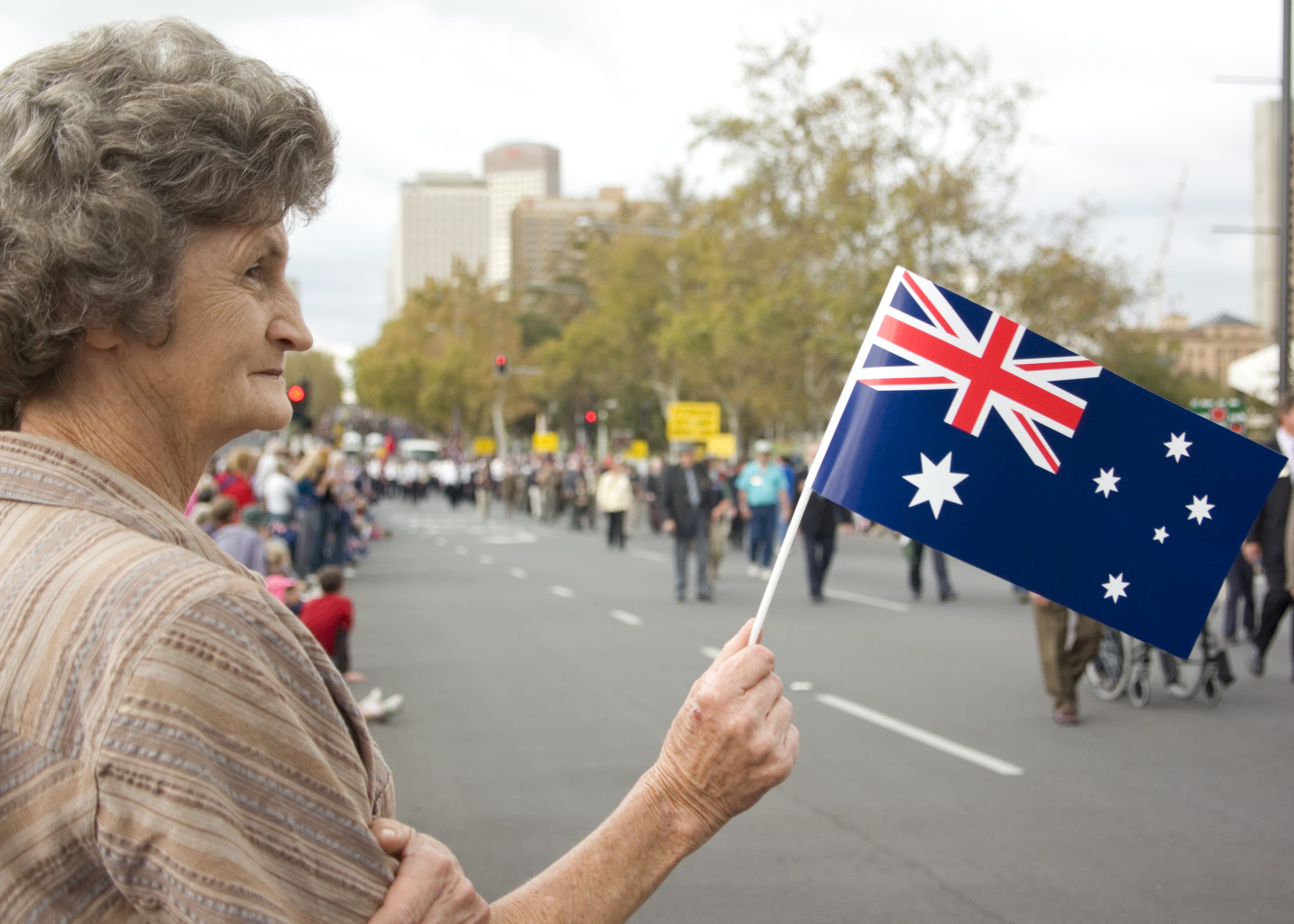 An older woman holding an Australian flag at an Anzac Day parade