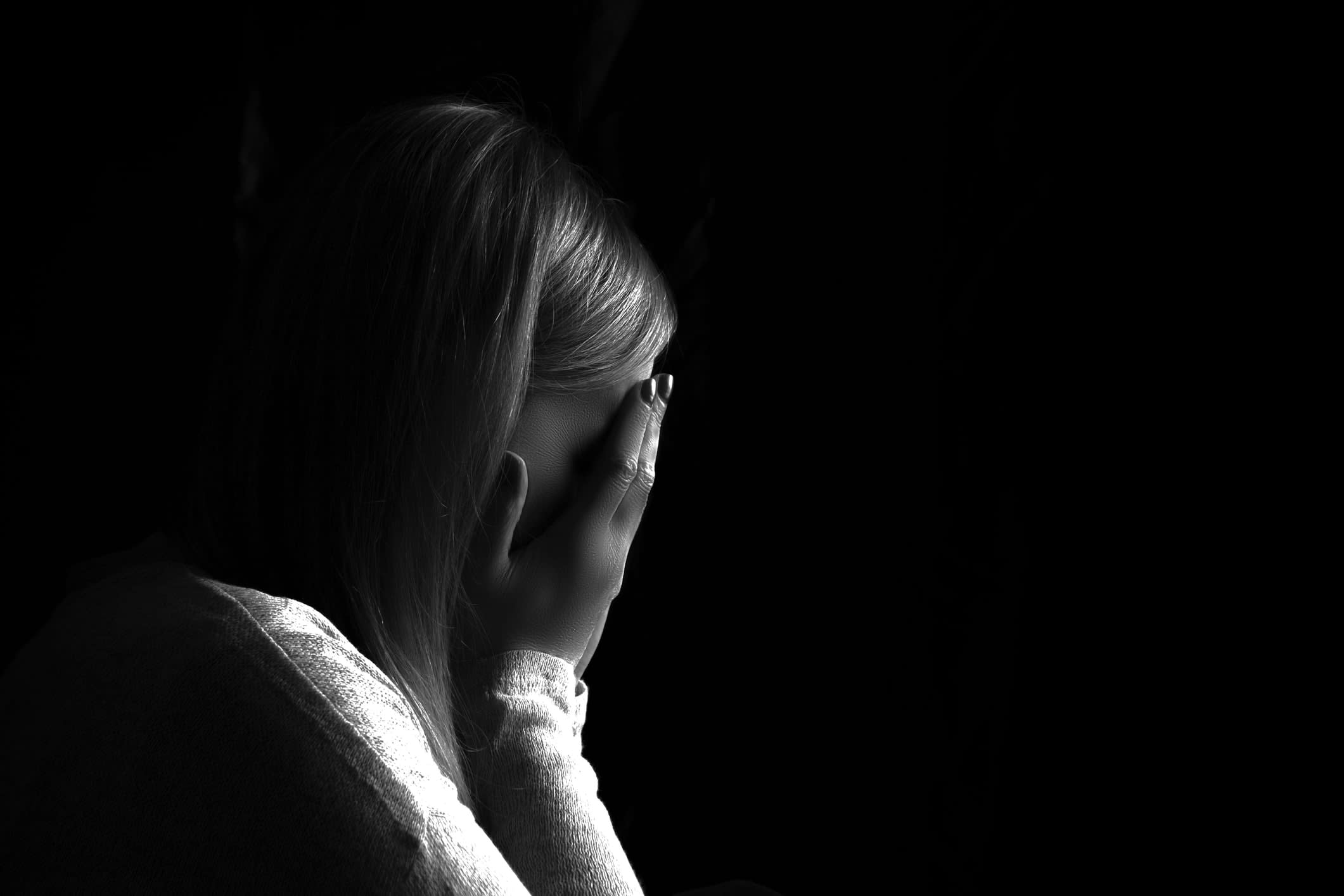 Side-on black-and-white image of a distraught woman holding her hands over her face