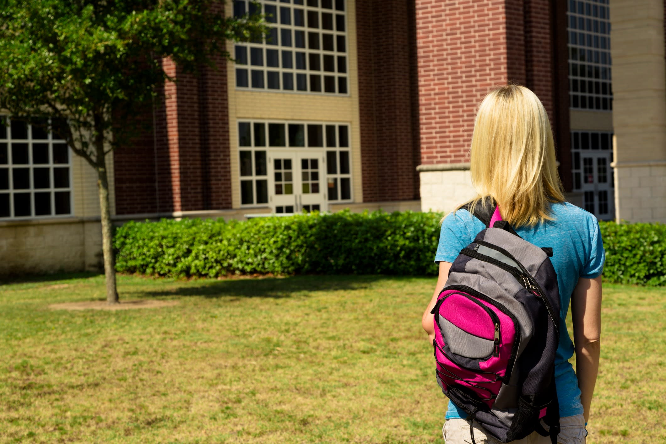 Young woman carrying backpack walks across campus lawn.