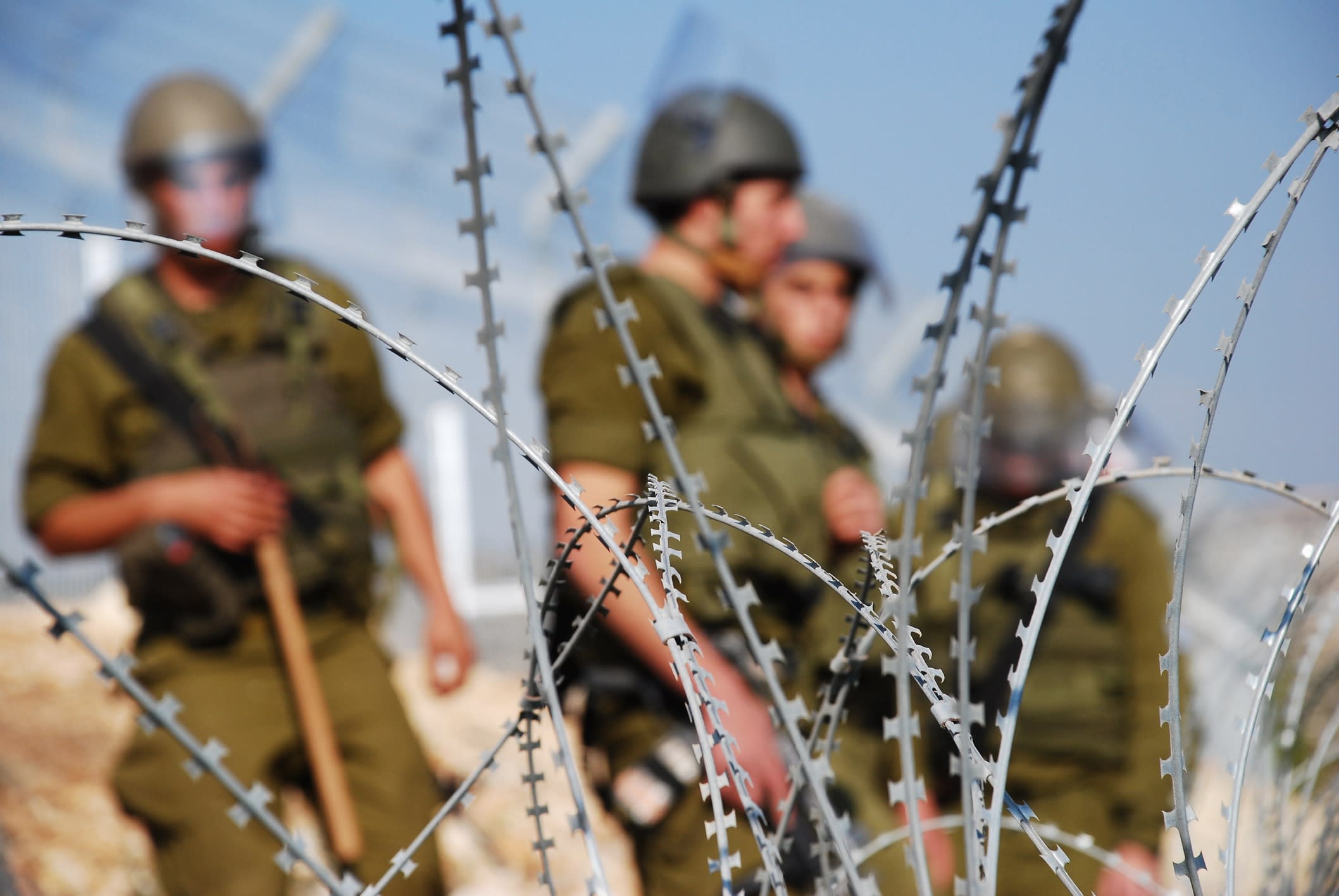 Israeli soldiers behind barbed wire fence.