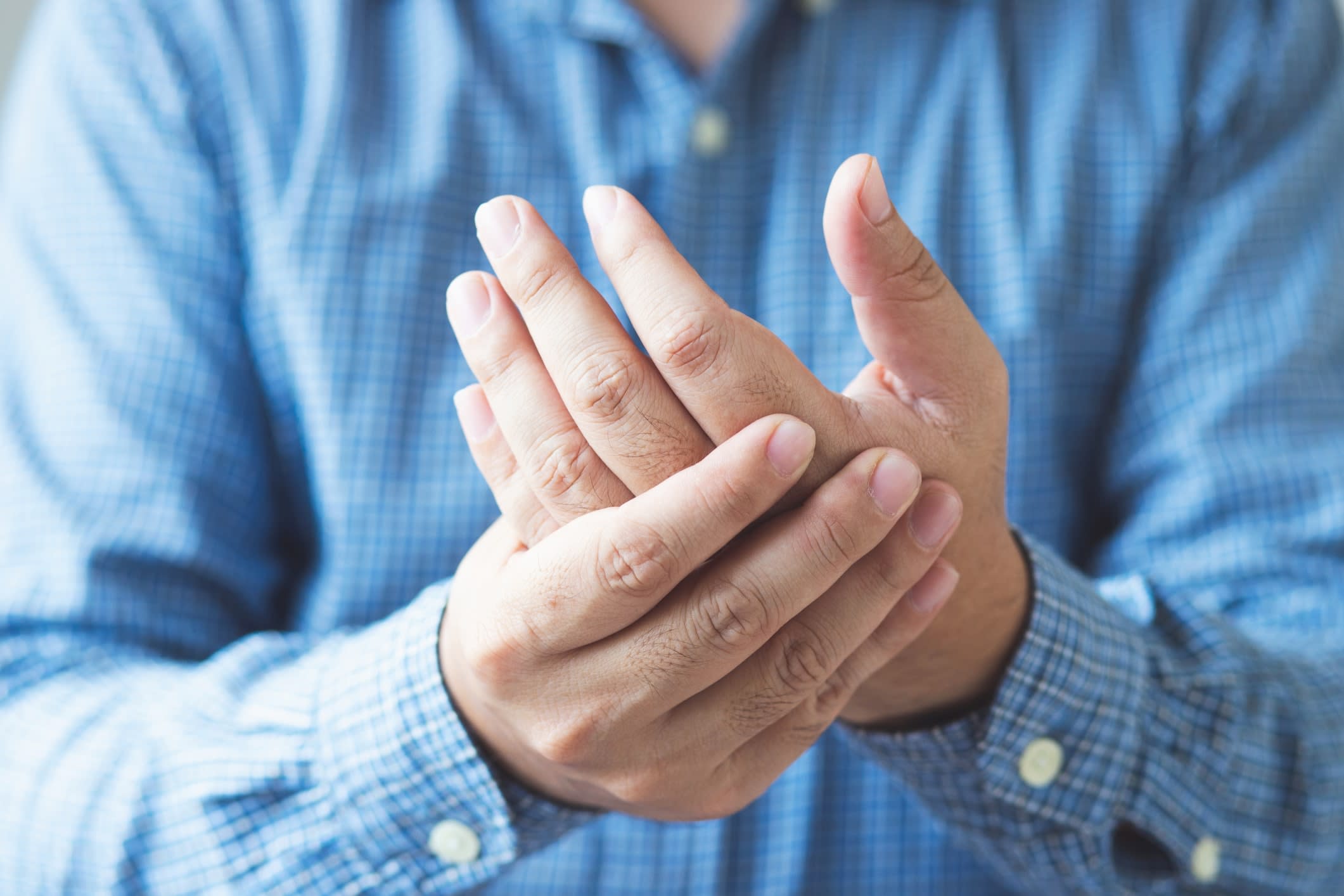 A man cradling his hand in his opposite hand, indicating arthritis pain