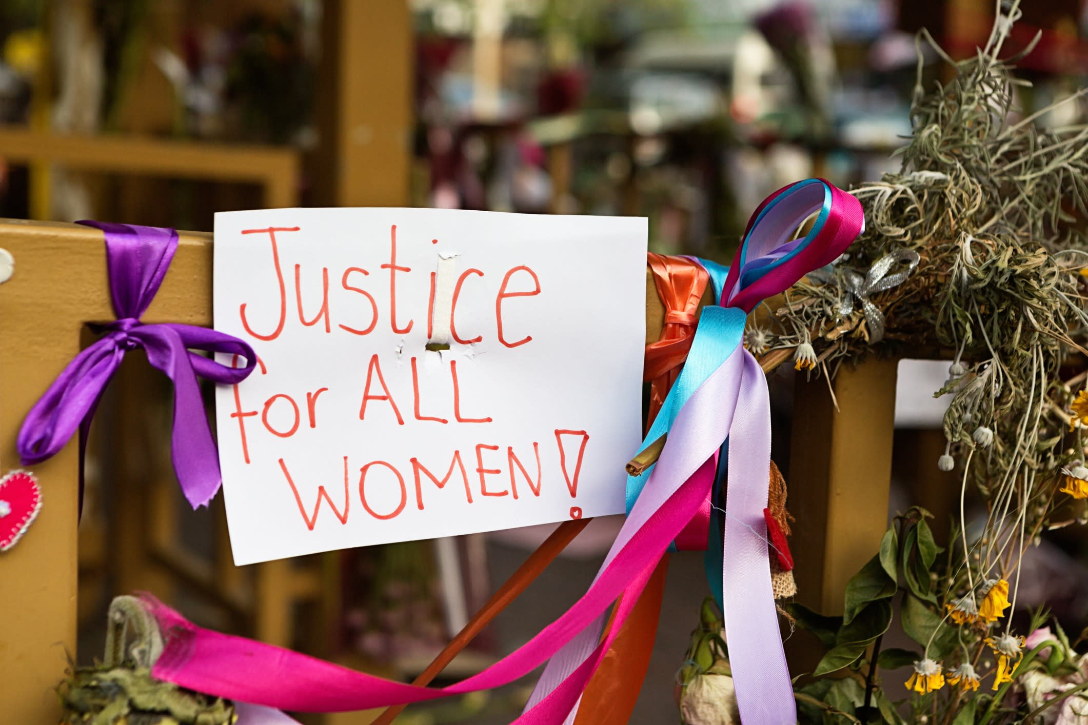 A hand-painted sign posted among flowers with the words 'Justice for all women' written on it.