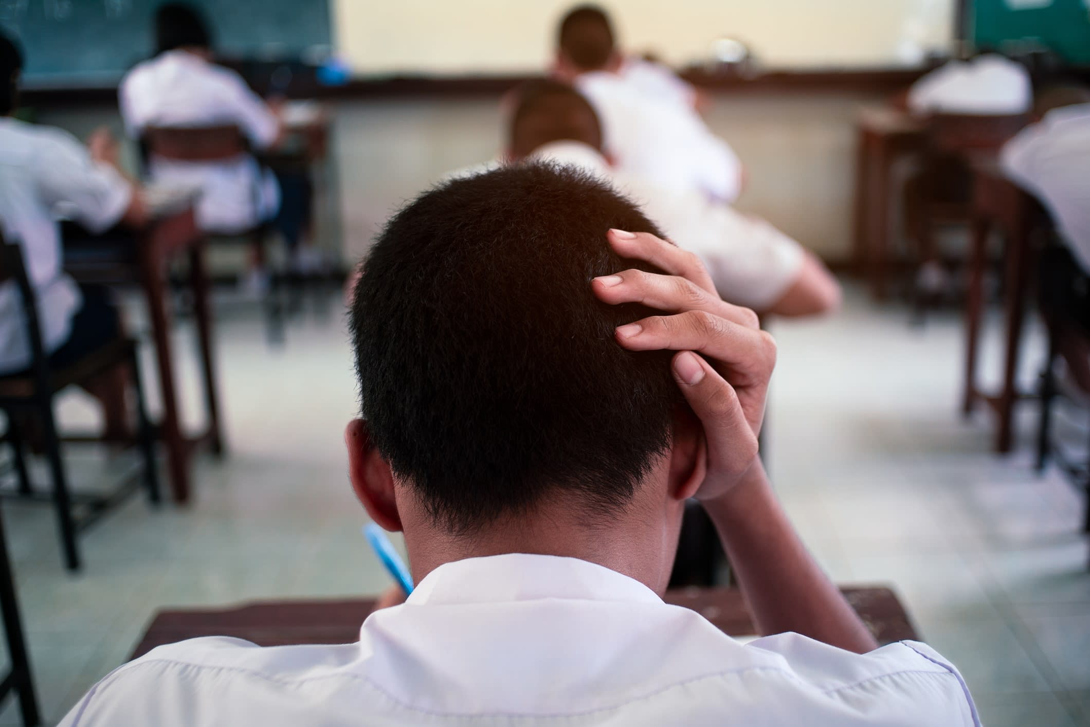 Stress-looking student with hand on head photographed from behind in a classroom 