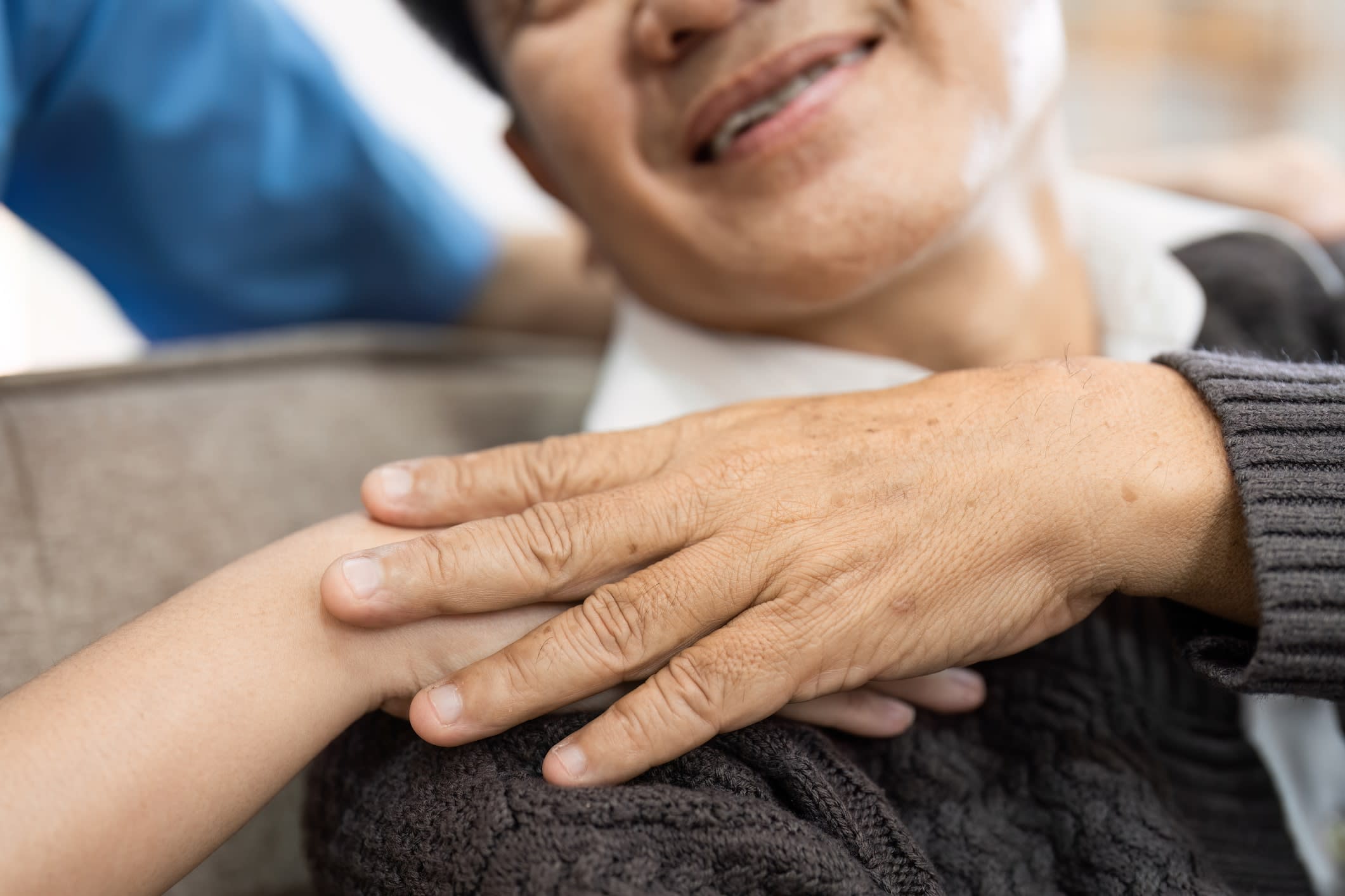 Close-up of a smiling older Asian woman putting her hand on the hand of a younger person on her shoulder