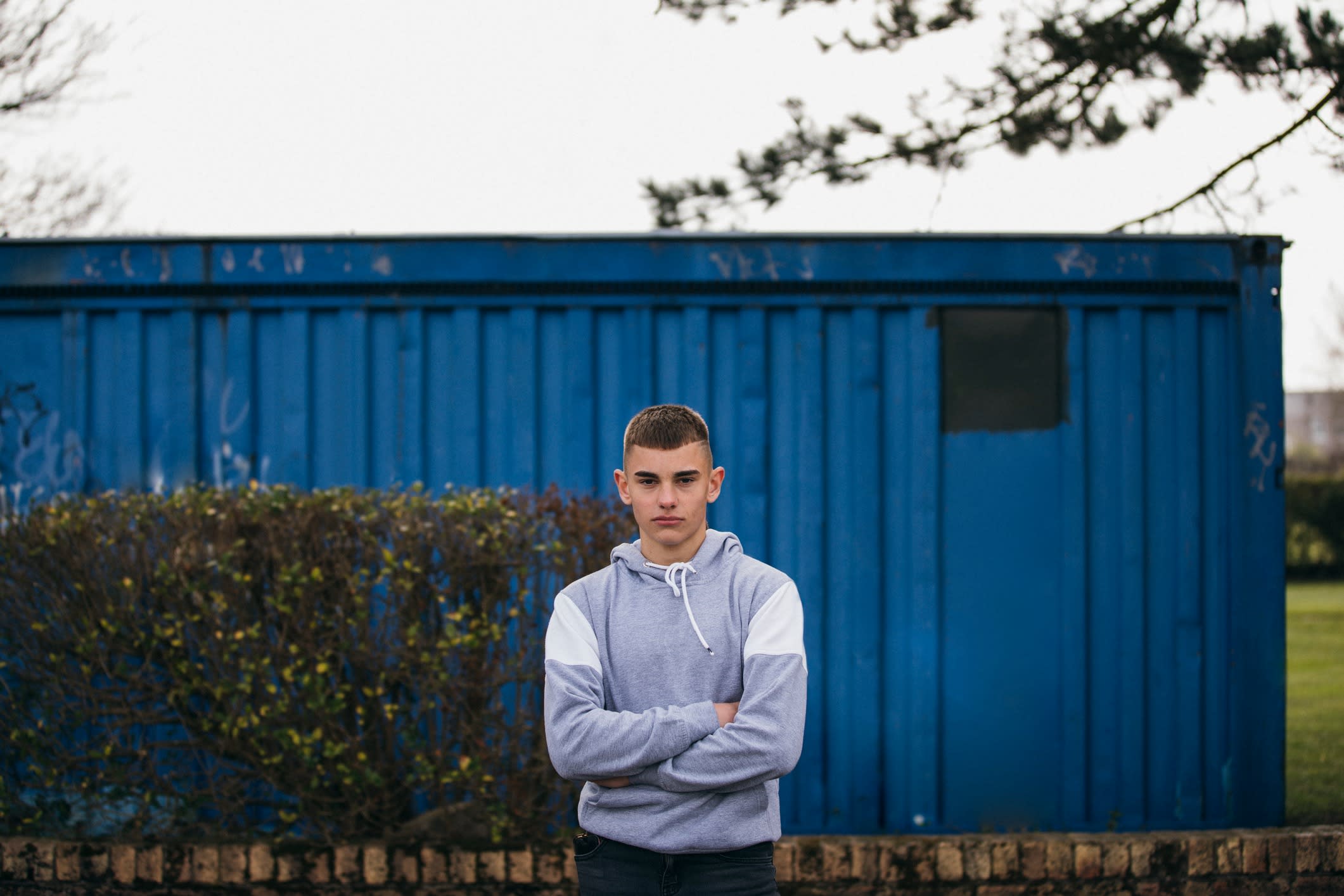 Teenage boy standing in front of a blue shed.