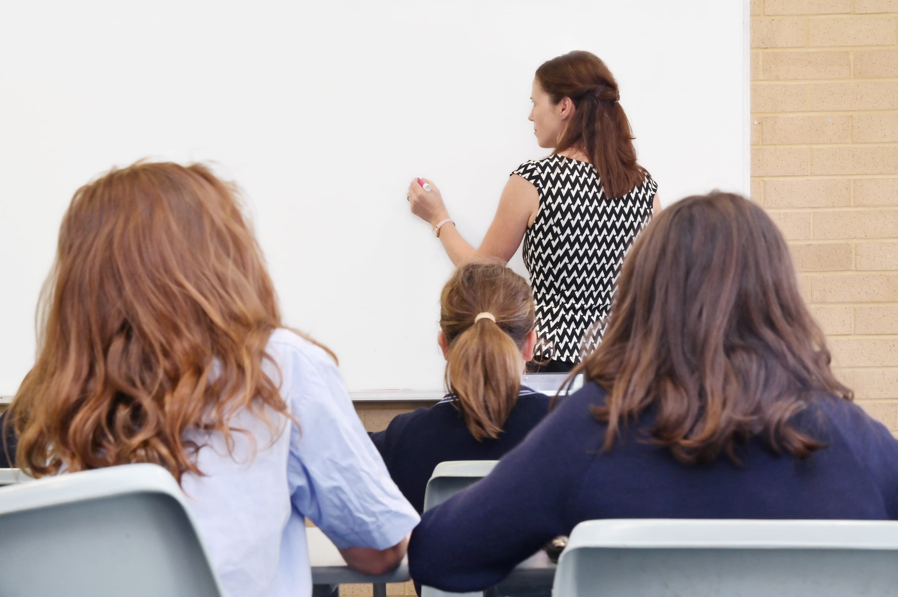 A female teacher writes on a whiteboard as female students look on