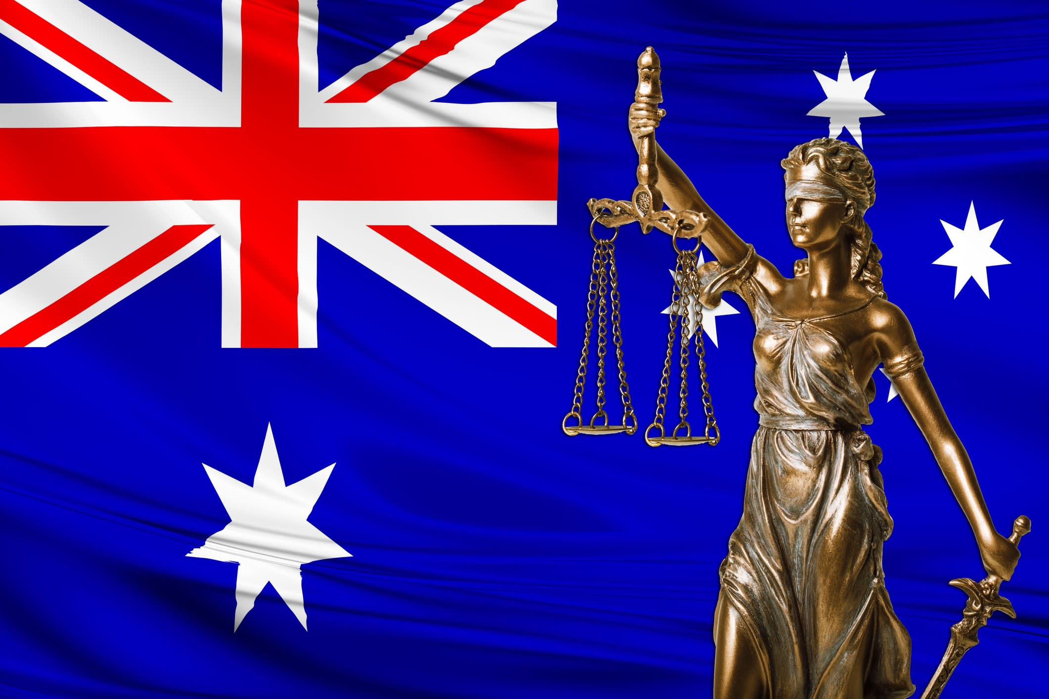 Lady justice statue holding scales with Australian flag in the background