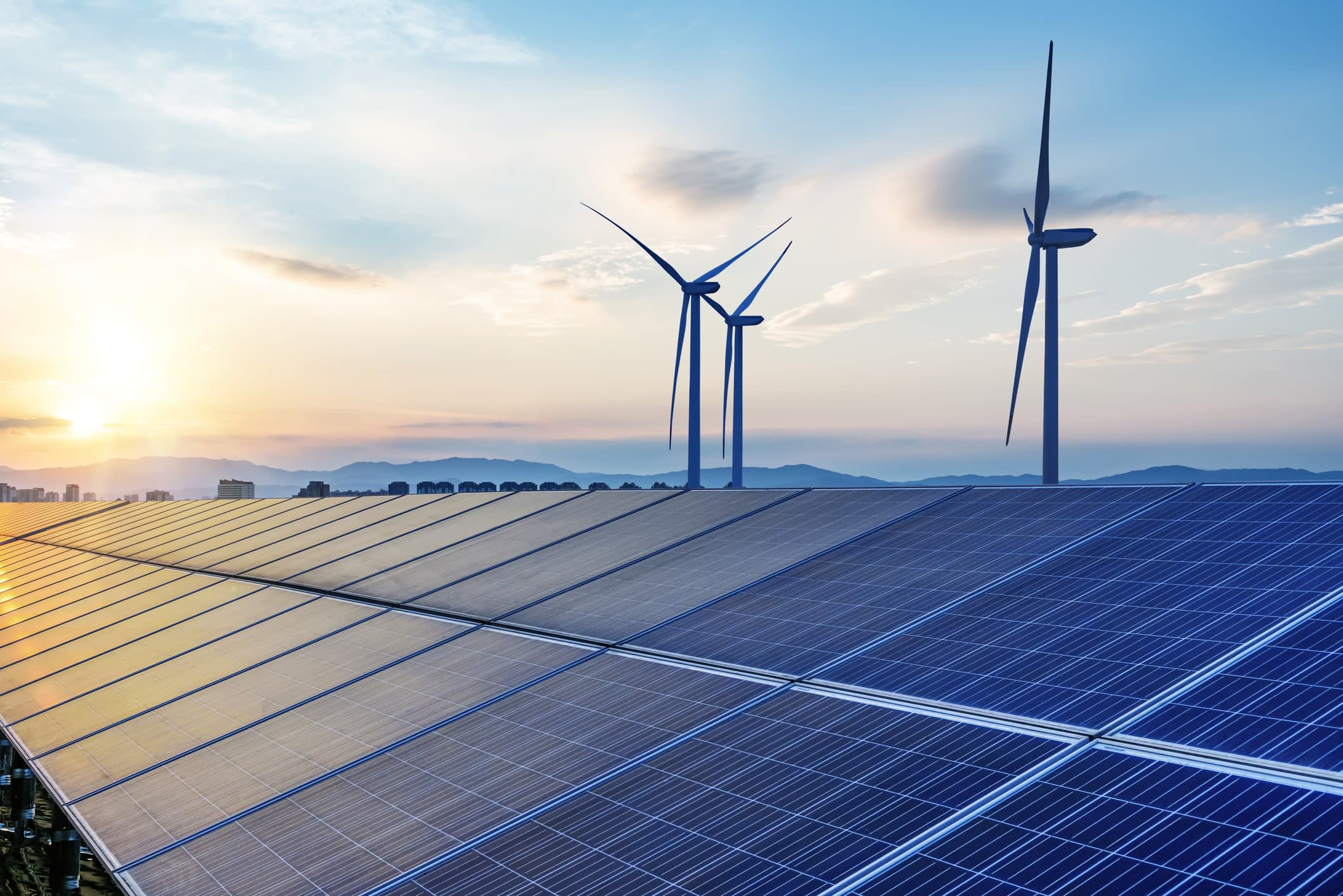Solar panel array at dusk, with wind turbines in the background