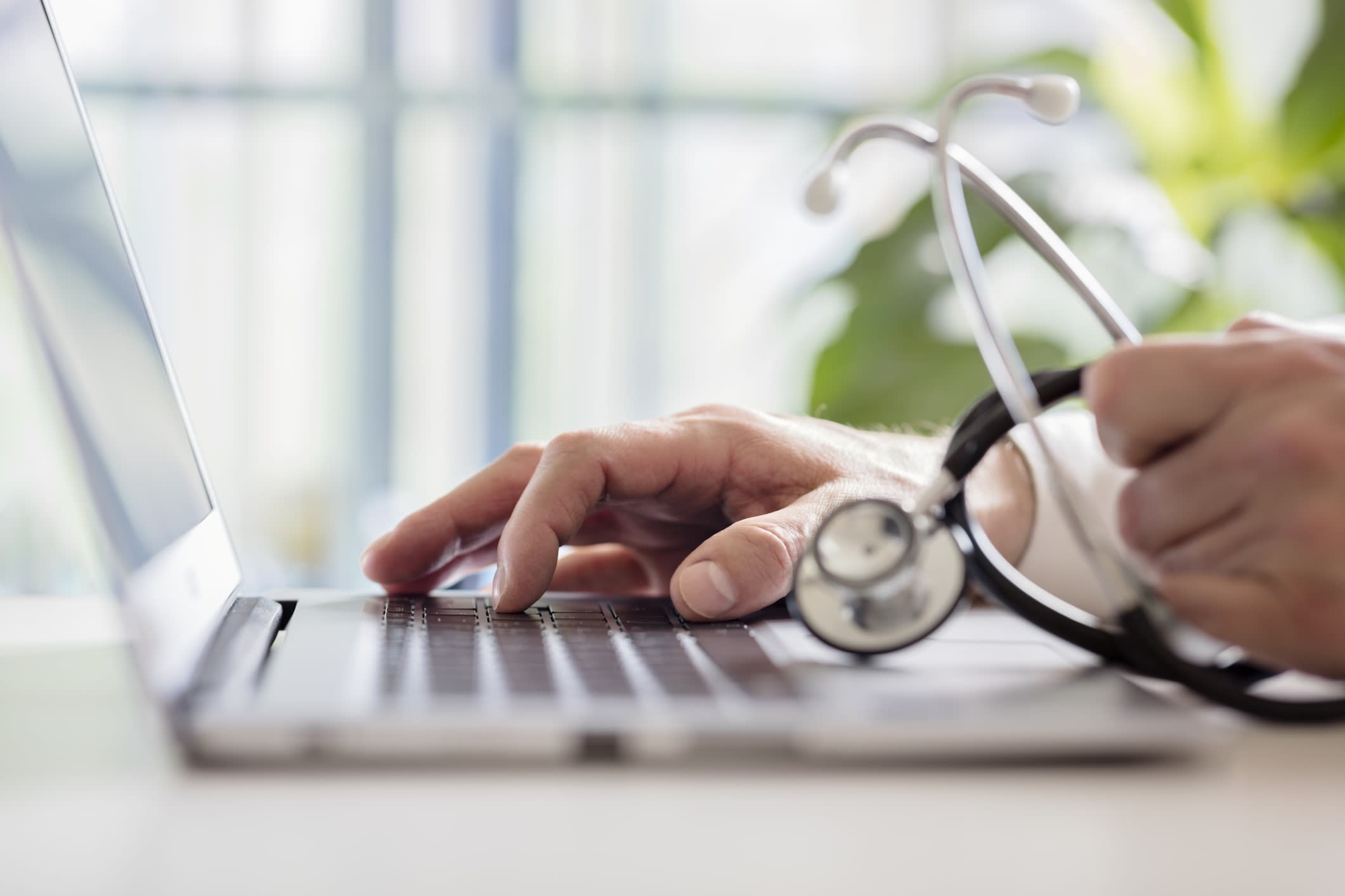 Doctor working on a laptop, holding a stethoscope