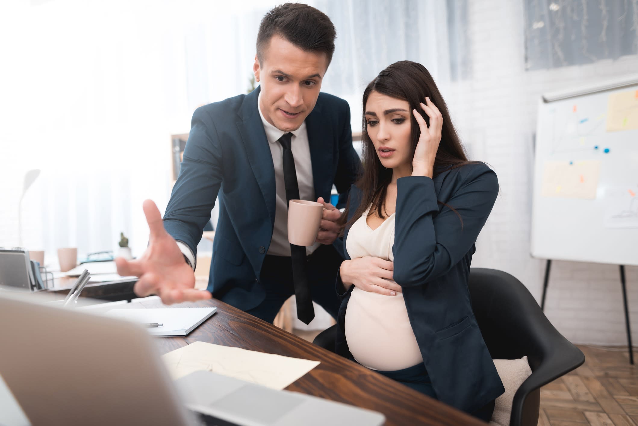 The boss yells at a pregnant employee who did not work. Pregnant woman grabs her head and stomach from nerves.