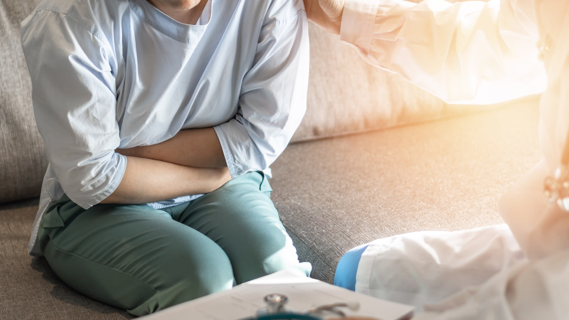 A woman in discomfort sitting on a couch clutching her stomach