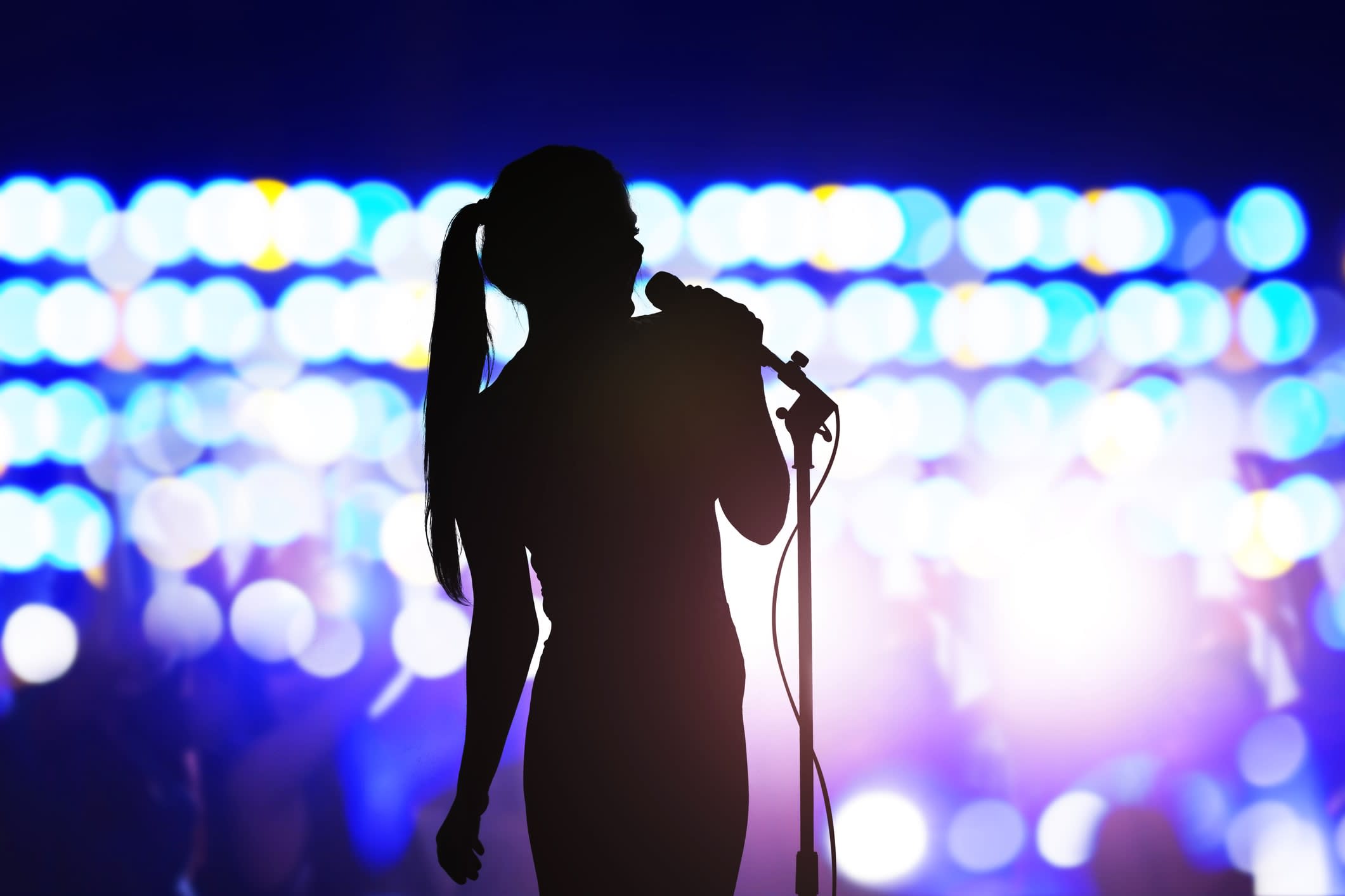 Silhouette of woman with microphone singing on concert stage in front of crowd