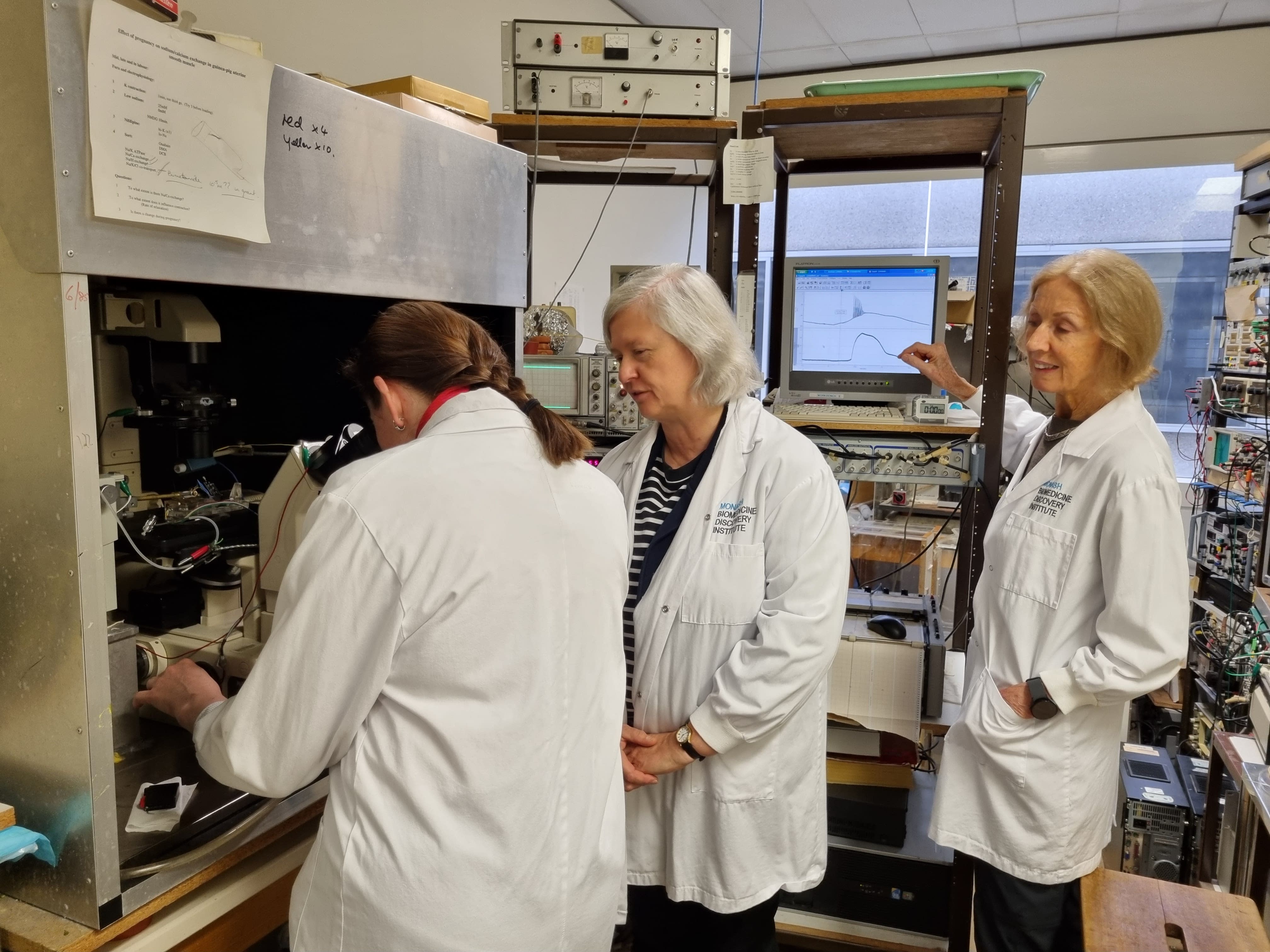 Dr Olesia Moroz looks into a microscope as Associate Professor Marianne Tare and Emeritus Professor Helena Parkington look on 