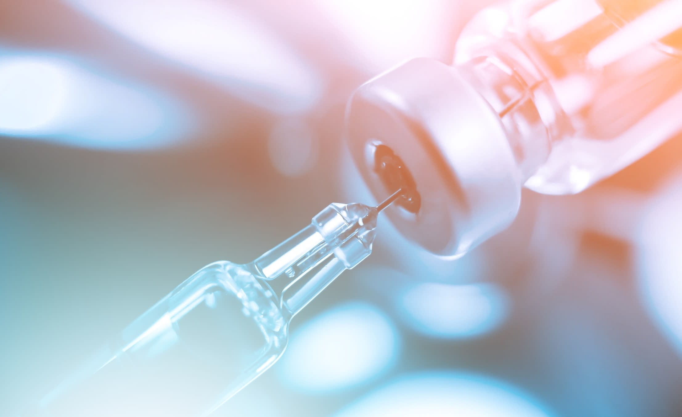 A syringe extracting vaccine from a vial