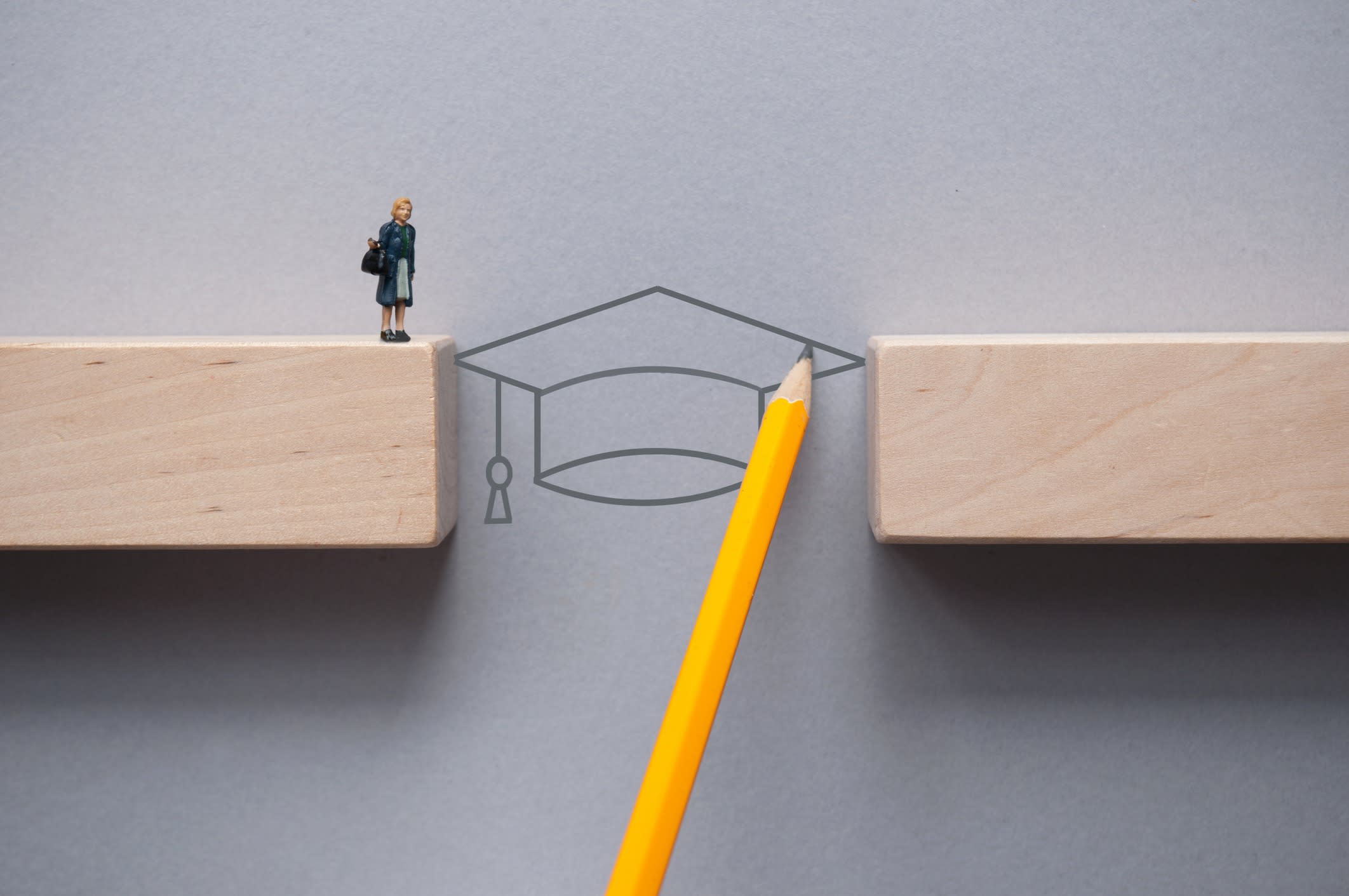 Academic cap bridges the divide between two blocks, allowing figurine to step across.