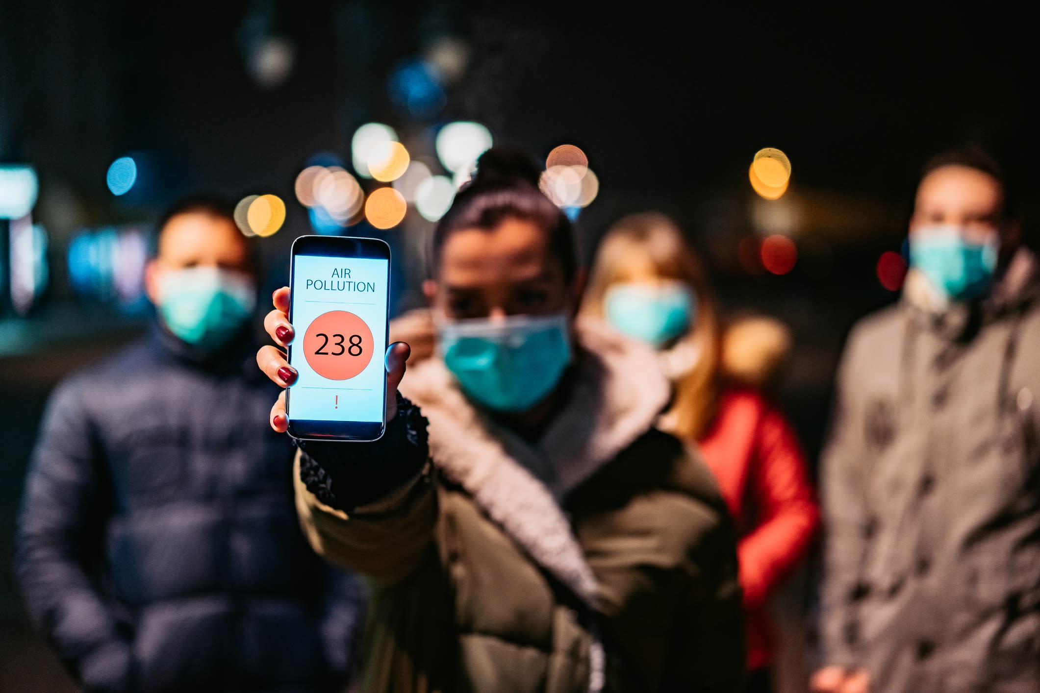 Young woman with pollution mask showing mobile pollution application in which is shown high air pollution in city.