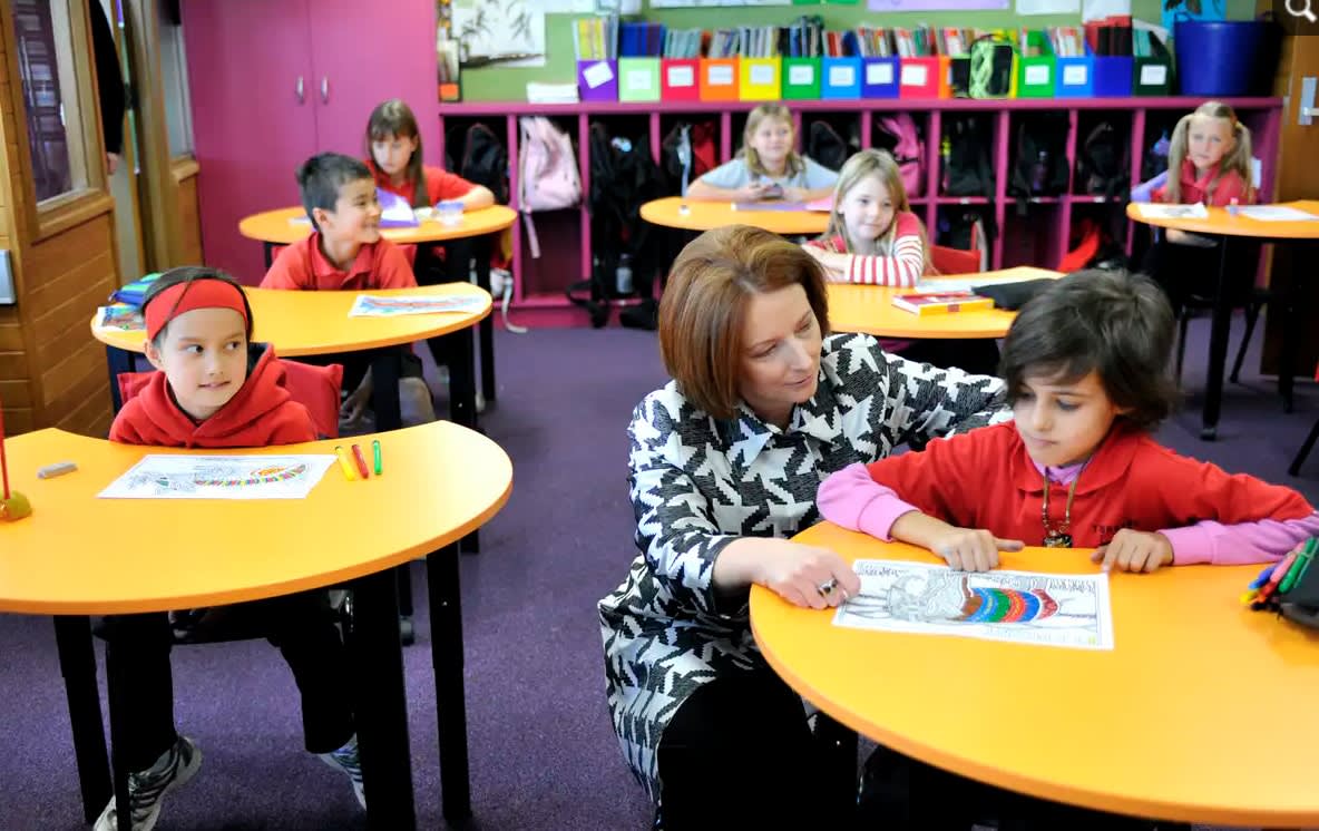 Former prime minister and education minister Julia Gillard in a primary school classroom, crouches down next to a child at a desk