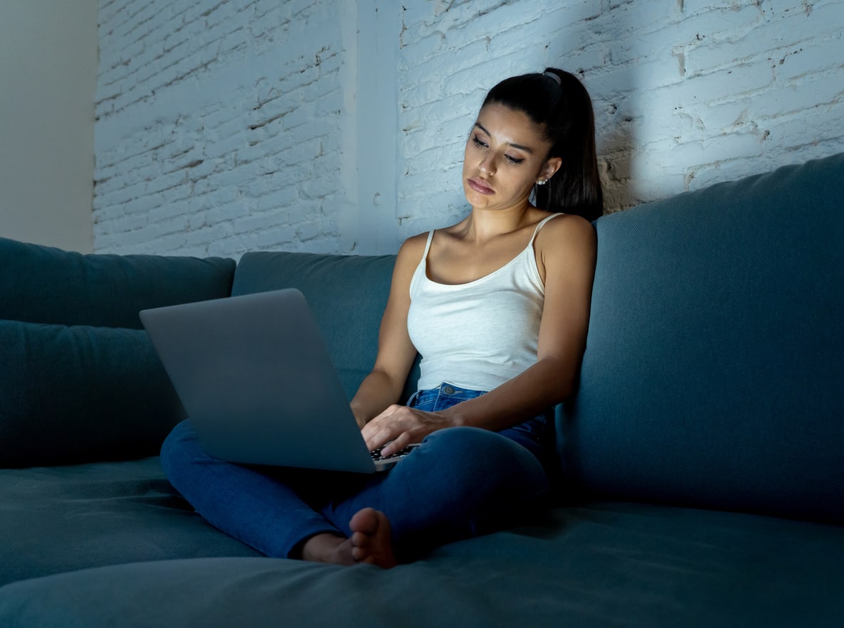 Woman cross-legged on a couch, staring at a laptop