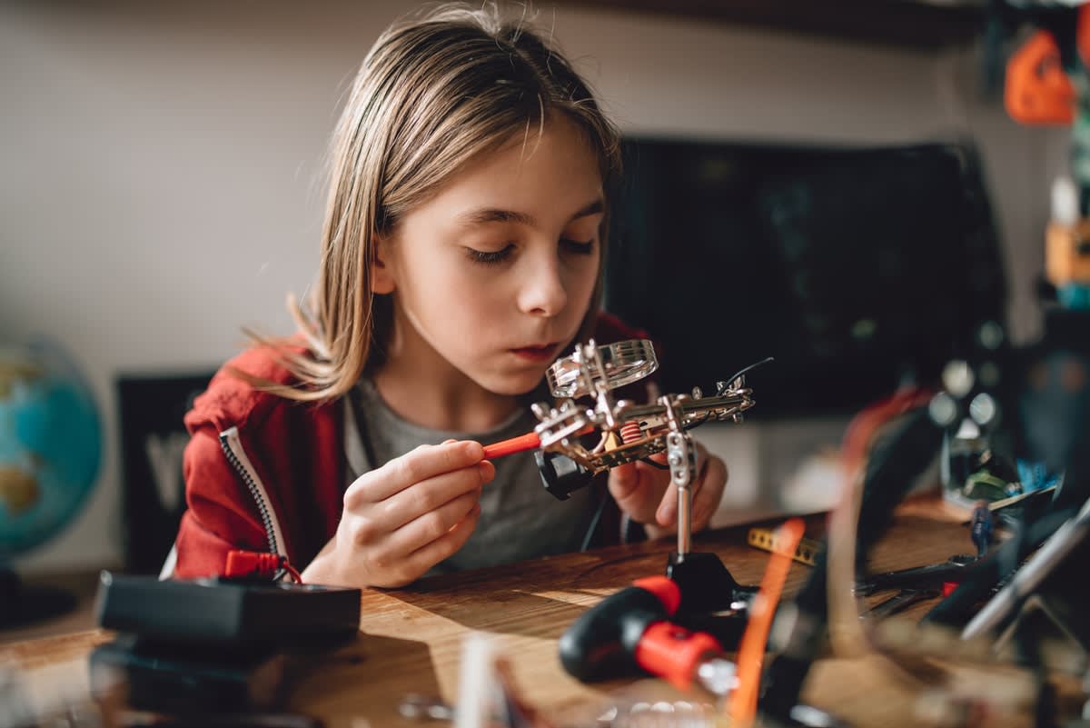 A young girl looking through a magnifying glass at a mechanical construction