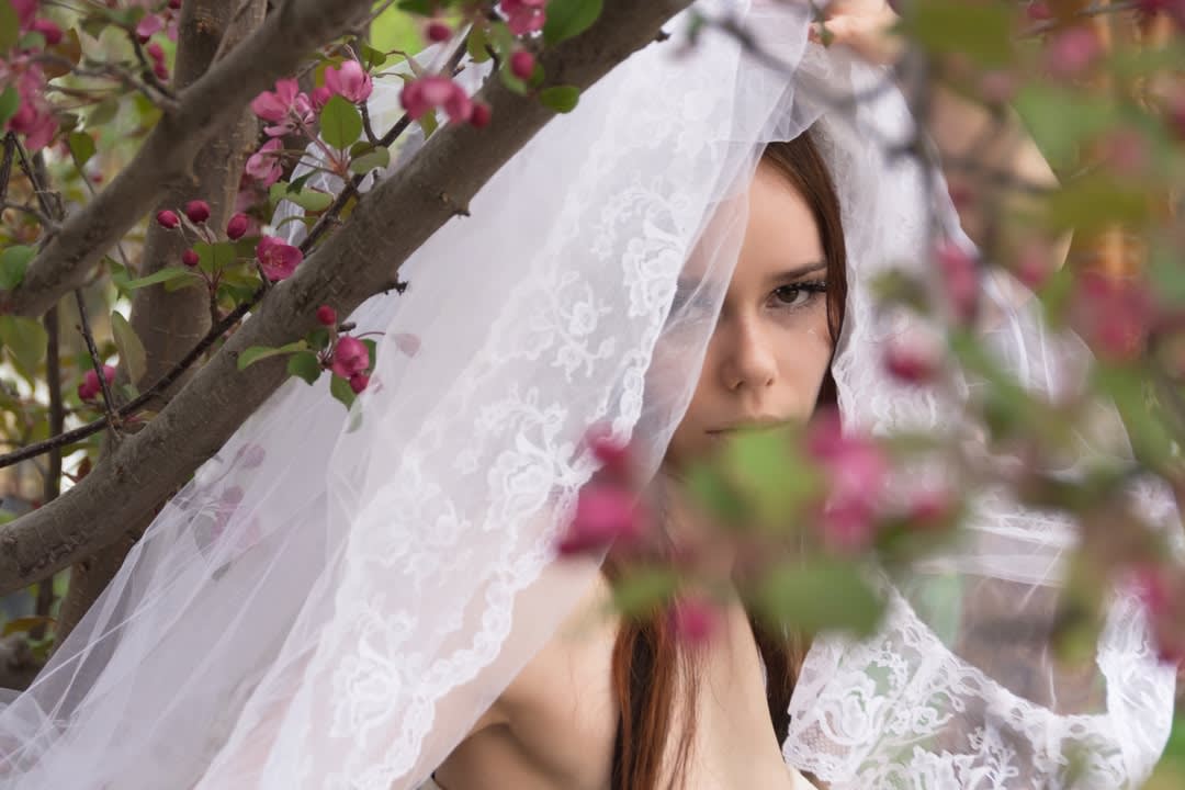 Young bride peeking from behind crab apple tree.