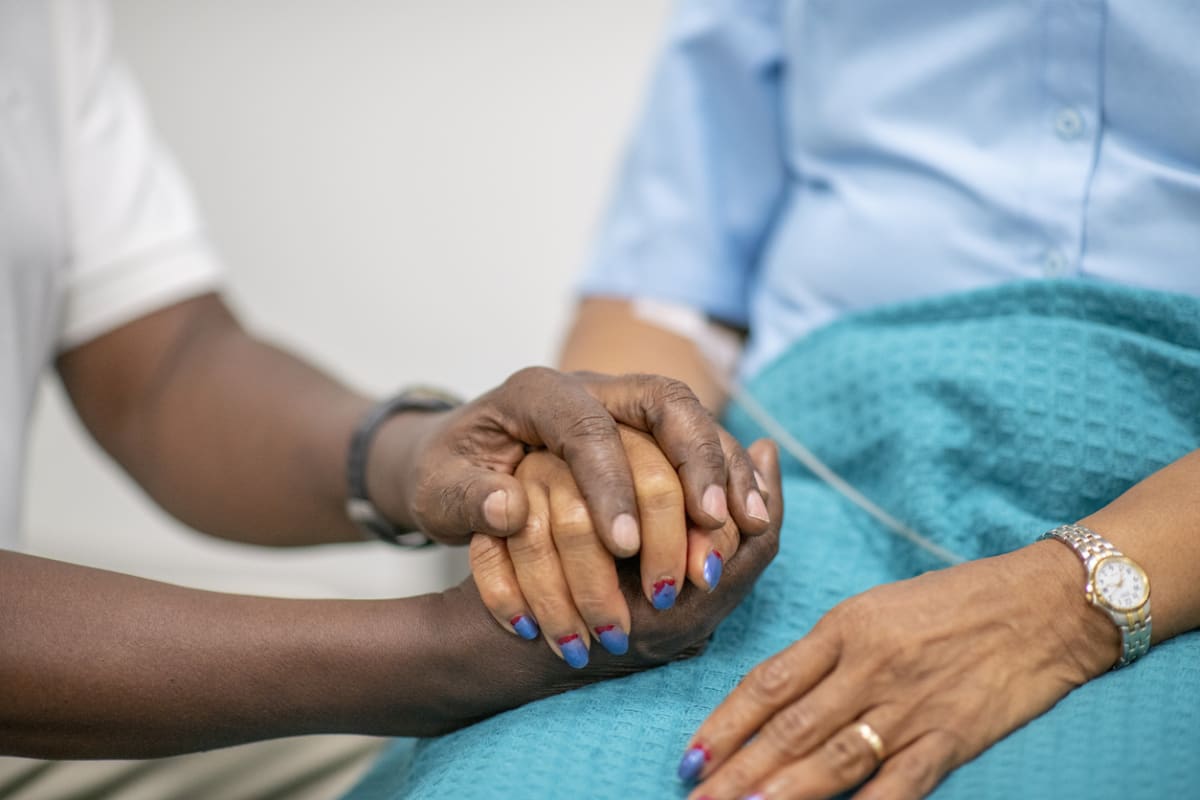 Close-up of care worker's hand, holding the hand of an elderly woman 