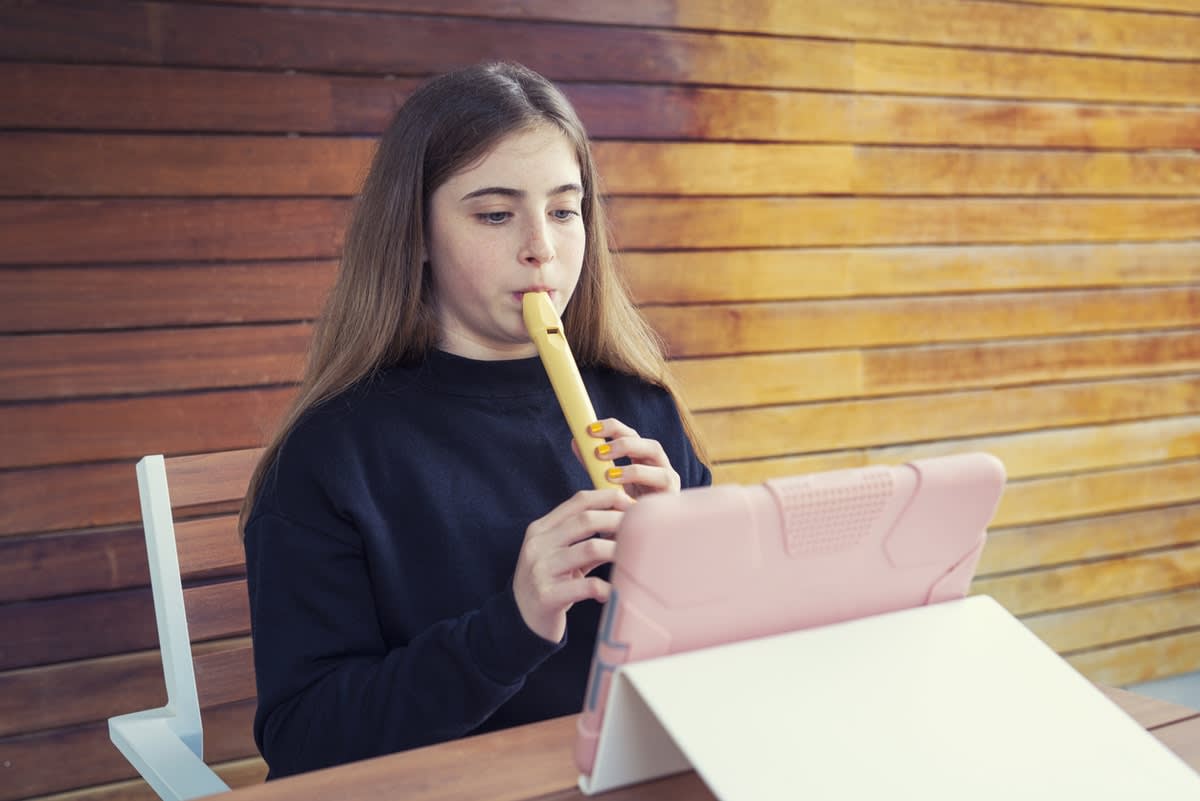 A girl sitting in a chair, playing flute in front of an iPad